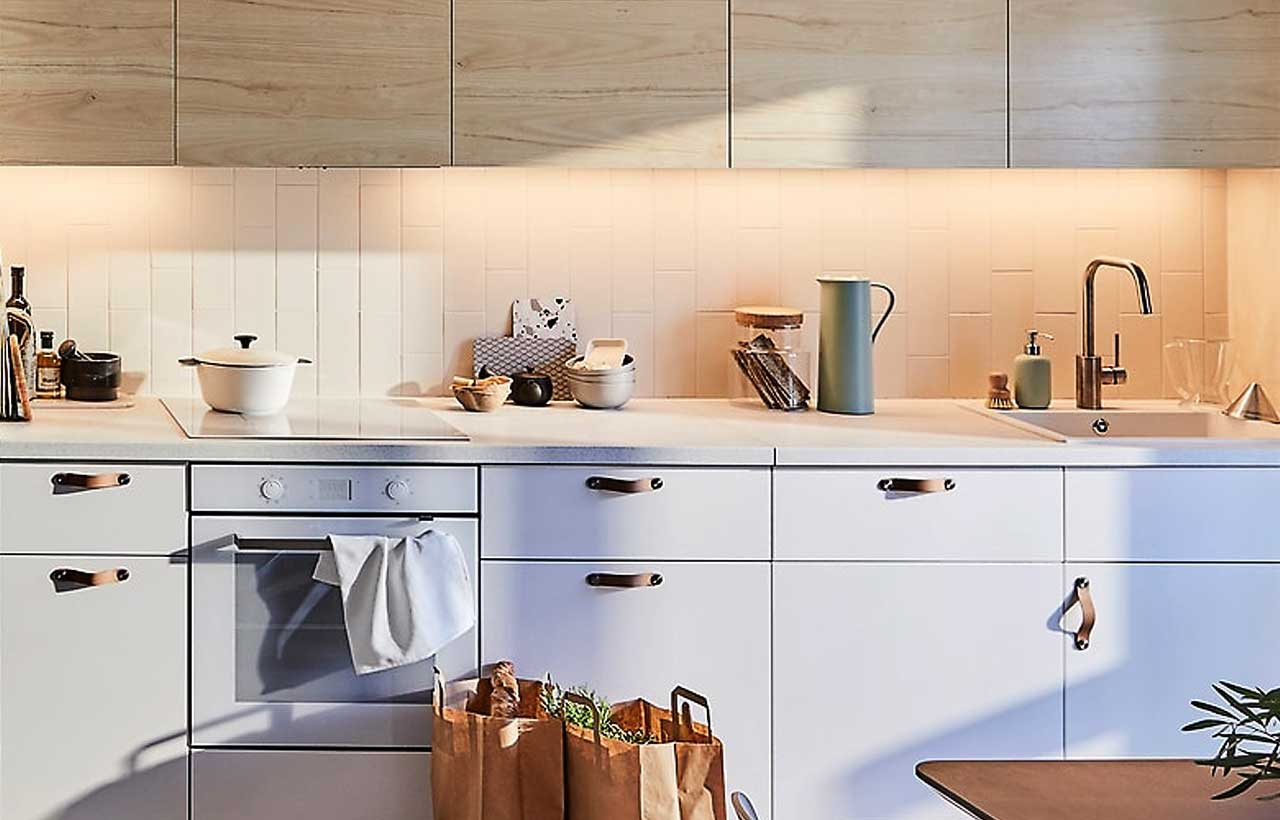A Sektion kitchen at dusk with warm under-cabinet lighting glowing onto a countertop, creating a cozy, inviting atmosphere