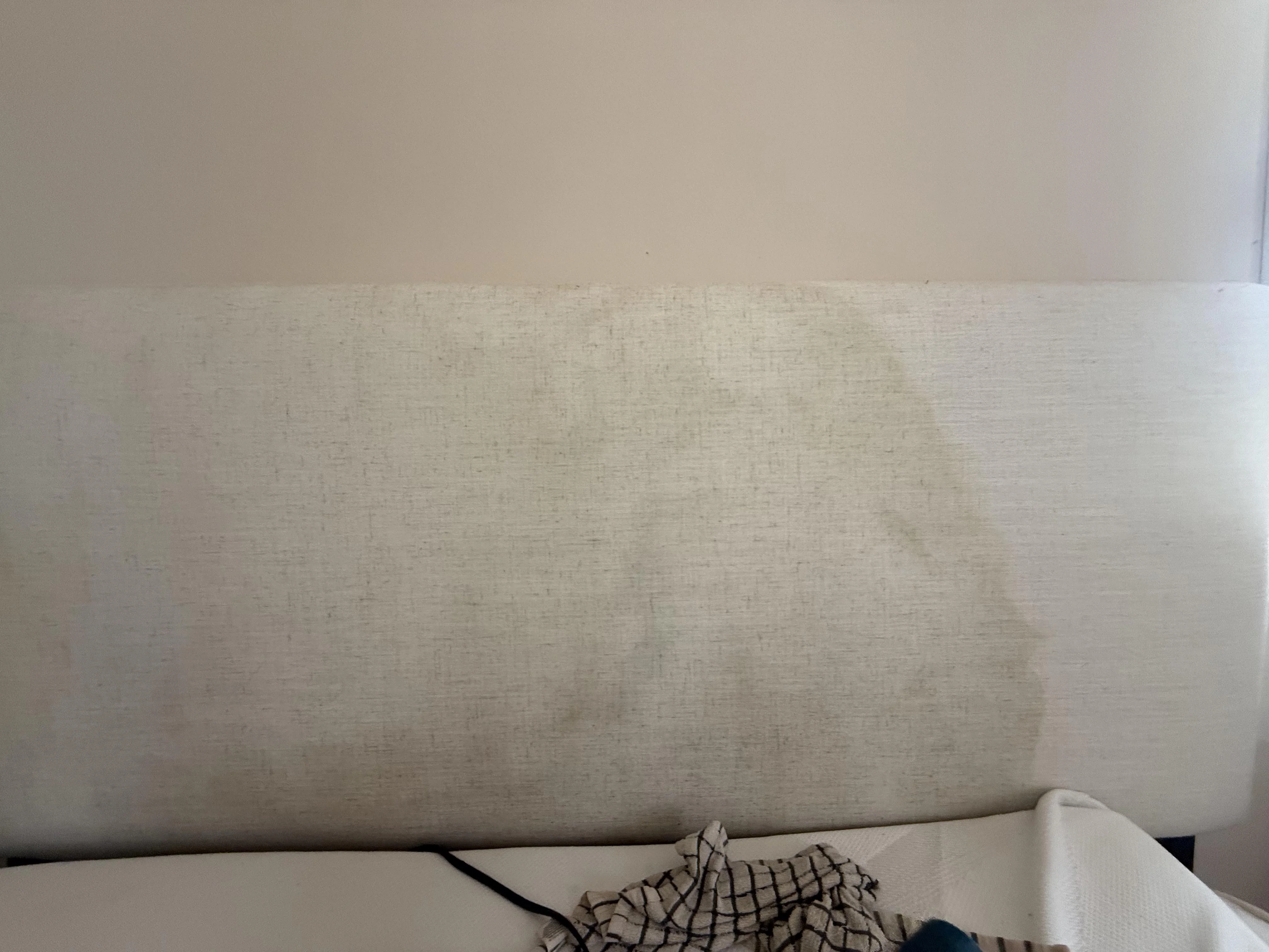 A bedroom wall with peeling paint and brownish water staining behind where a headboard sits, photographed straight on