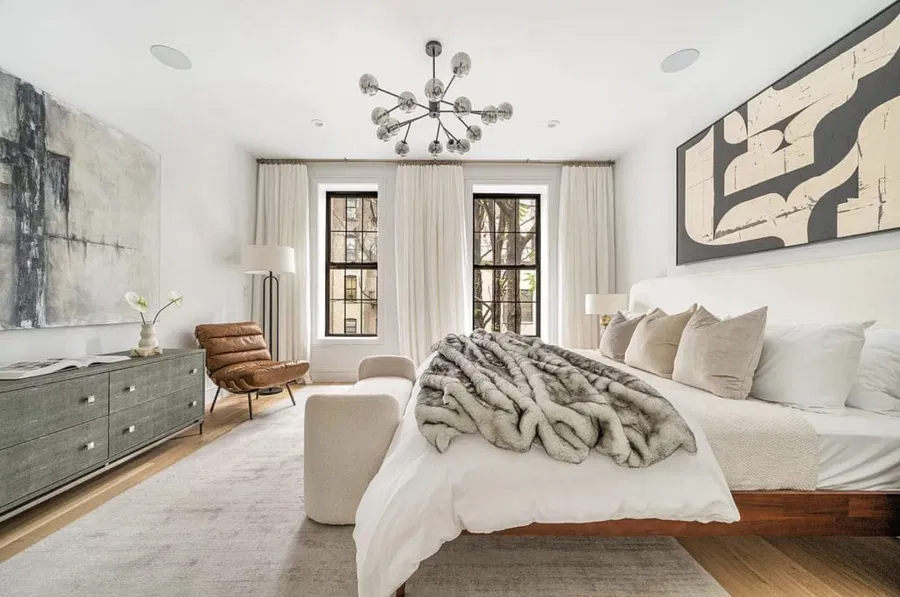 A bedroom with a softly draped linen fabric accent wall behind the bed, neutral bedding, and a vintage brass lamp, realistic interior photograph