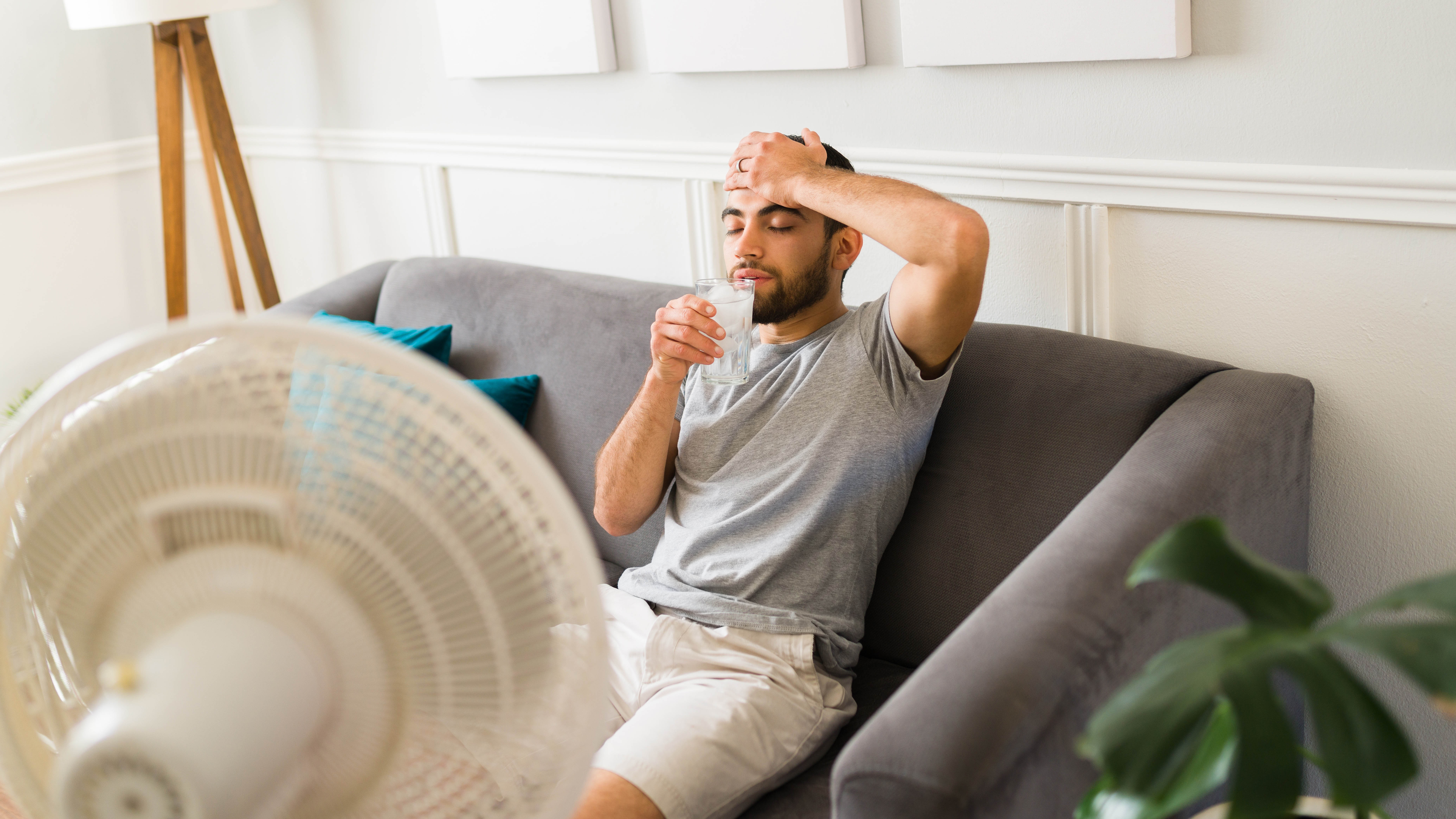 A box fan on the floor positioned a few feet away from upright sofa cushions so the airflow passes across the cushion surfaces, bright daytime interior