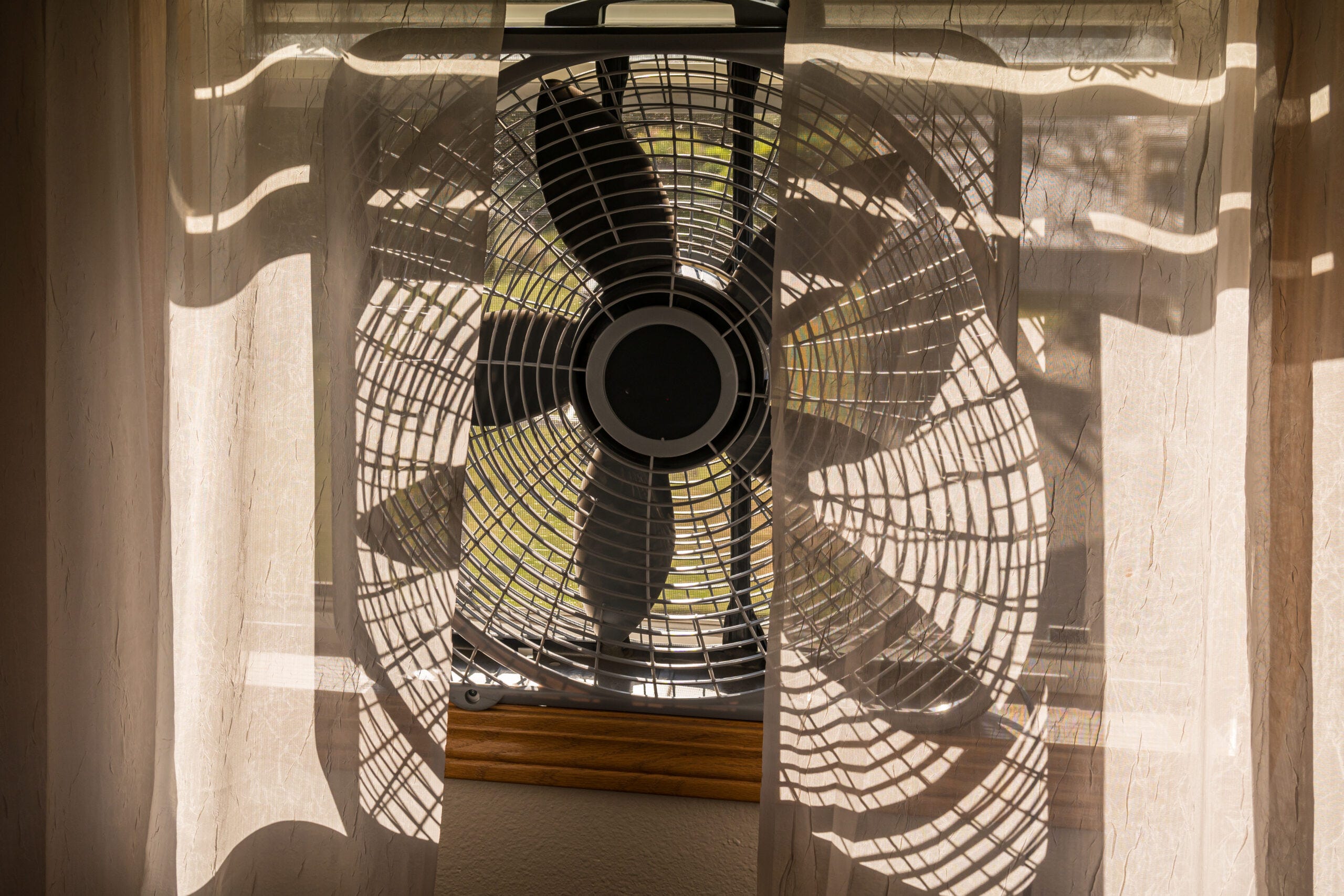 A box fan placed in an open window blowing air outward in a sunlit room