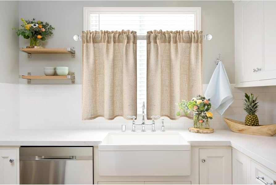 A bright kitchen with a window above a sink and simple cotton curtains ending at the window sill, with a faucet and countertop visible below