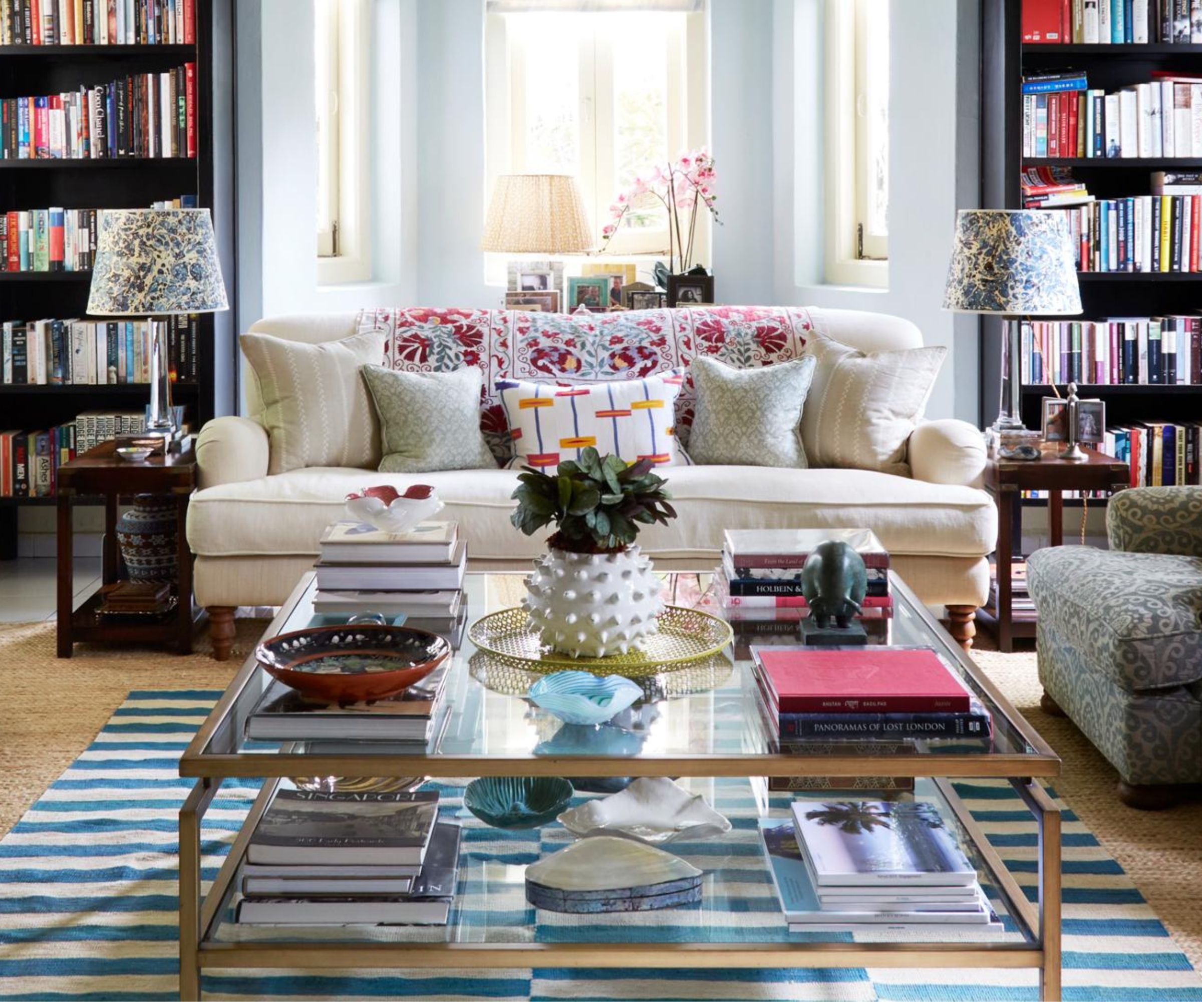A close photo of a coffee table with two oversized hardcover books stacked neatly beside a ceramic tray, with soft linen curtains in the background