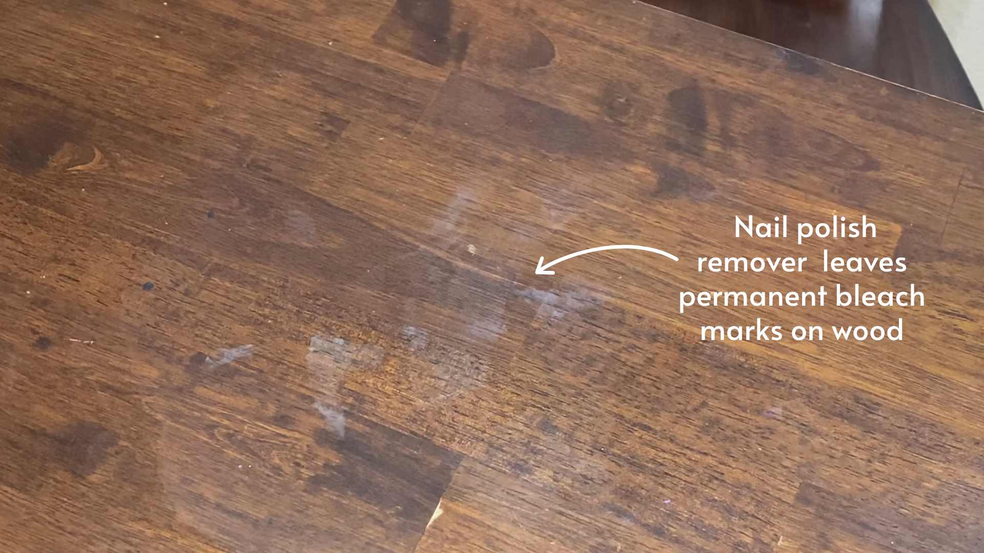 A close-up of a hand using a cotton swab with a small amount of acetone to lift a tiny spot of red nail polish from a finished wooden dresser top
