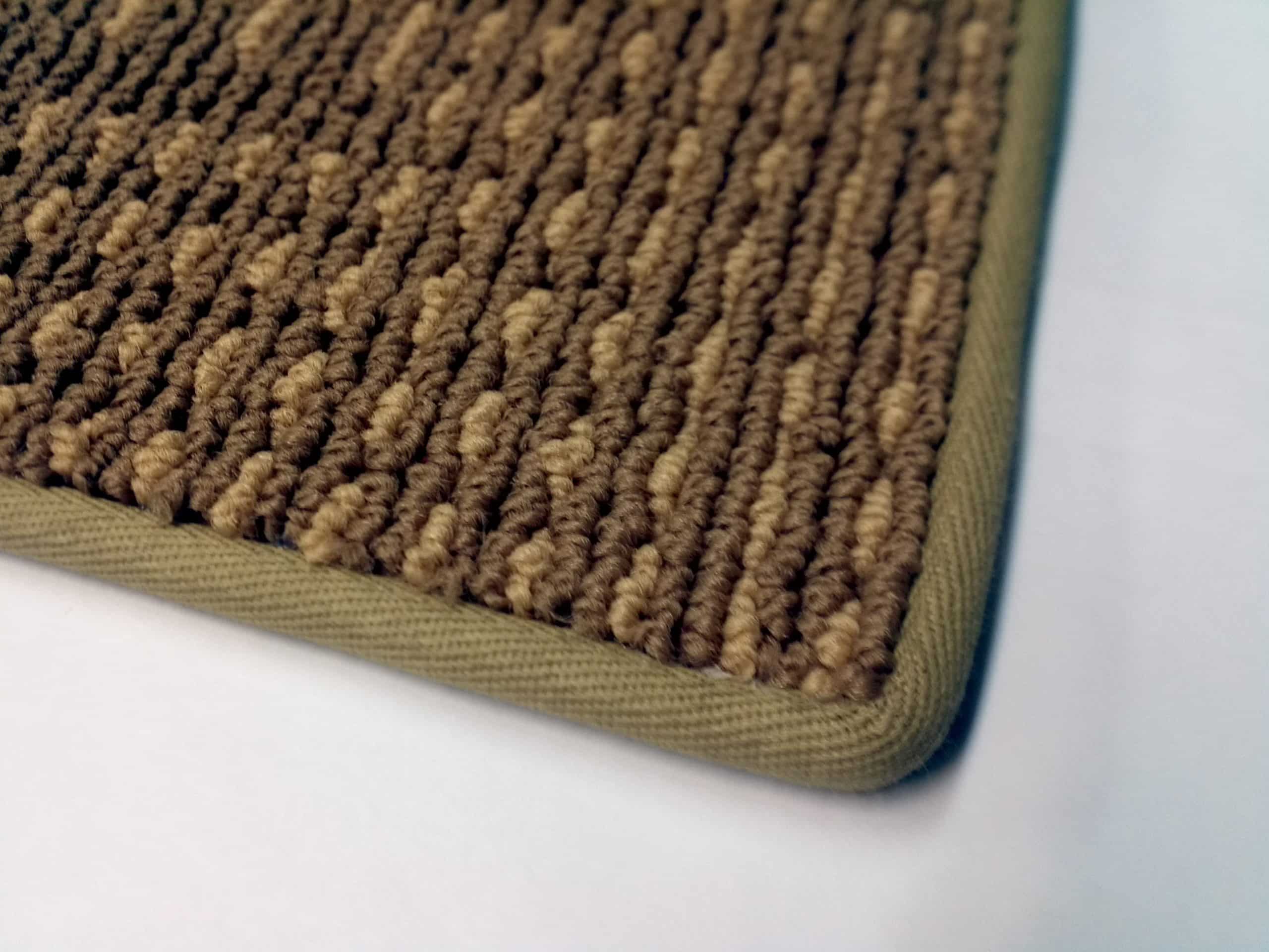 A close-up of a rug corner finished with a neat fabric binding tape in a neutral color, showing clean stitching along the edge