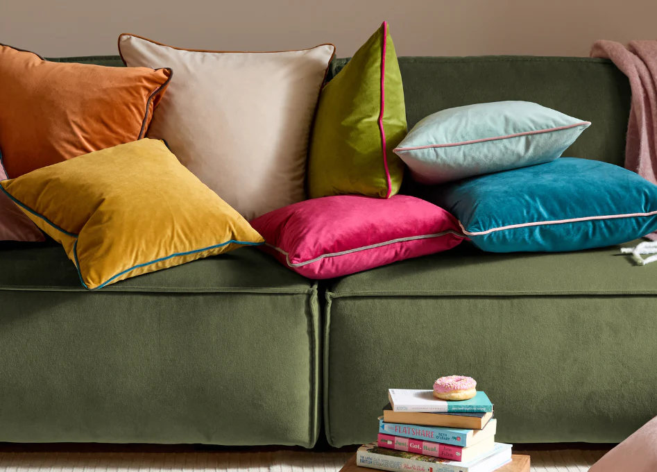 A close-up of hands blotting a fresh spill on a light-colored floor pillow cover with a clean white towel in a home setting
