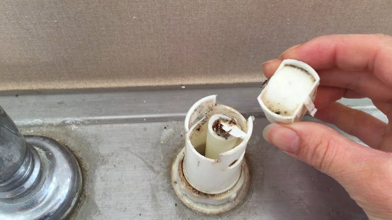 A close-up photo of a kitchen sink air gap with the cap being lifted off by hand, showing the small opening underneath