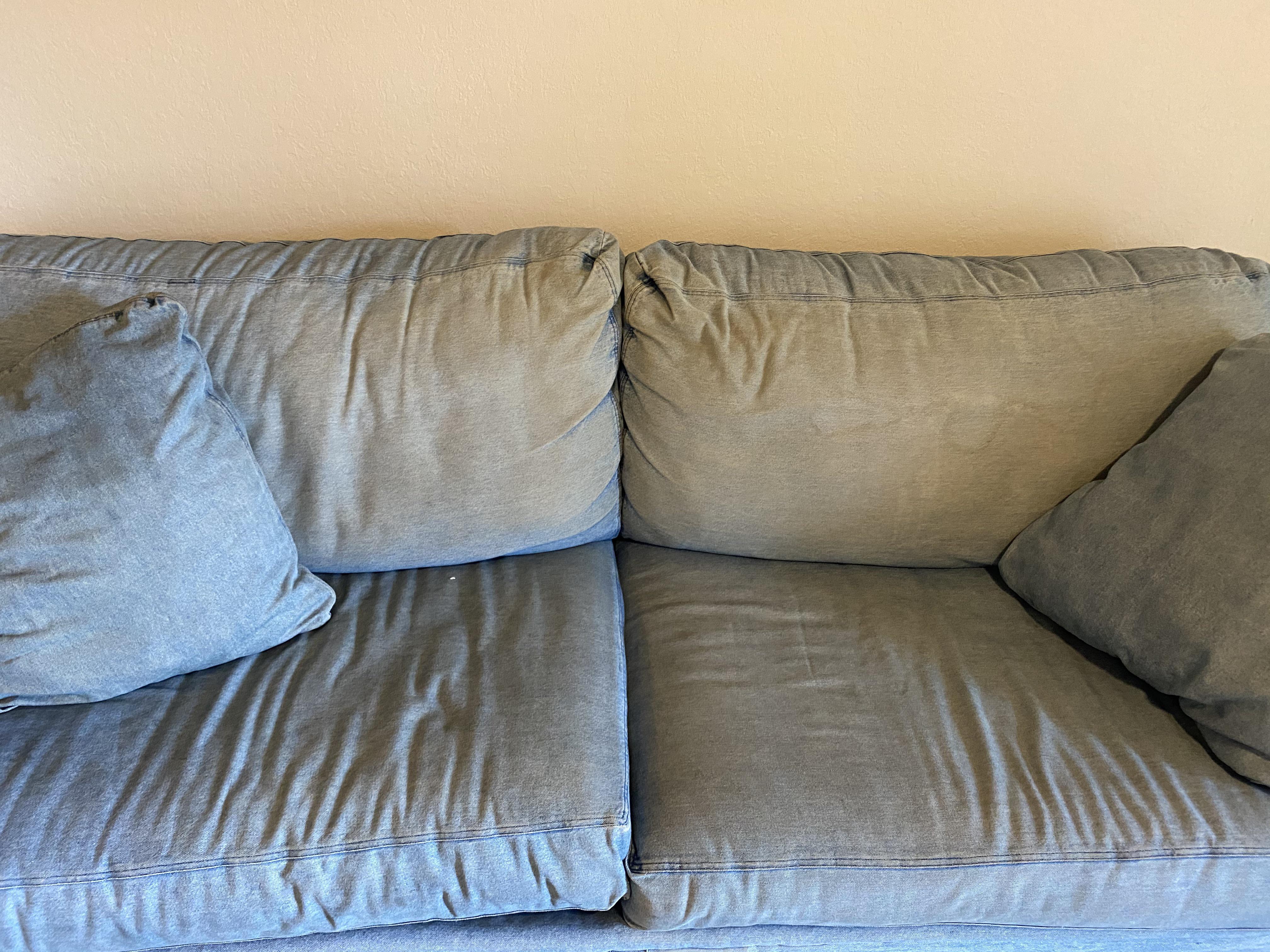 A close-up photo of a light beige sofa cushion with a faint blue denim dye transfer mark, with clean white cloths and a small bowl of cold water nearby