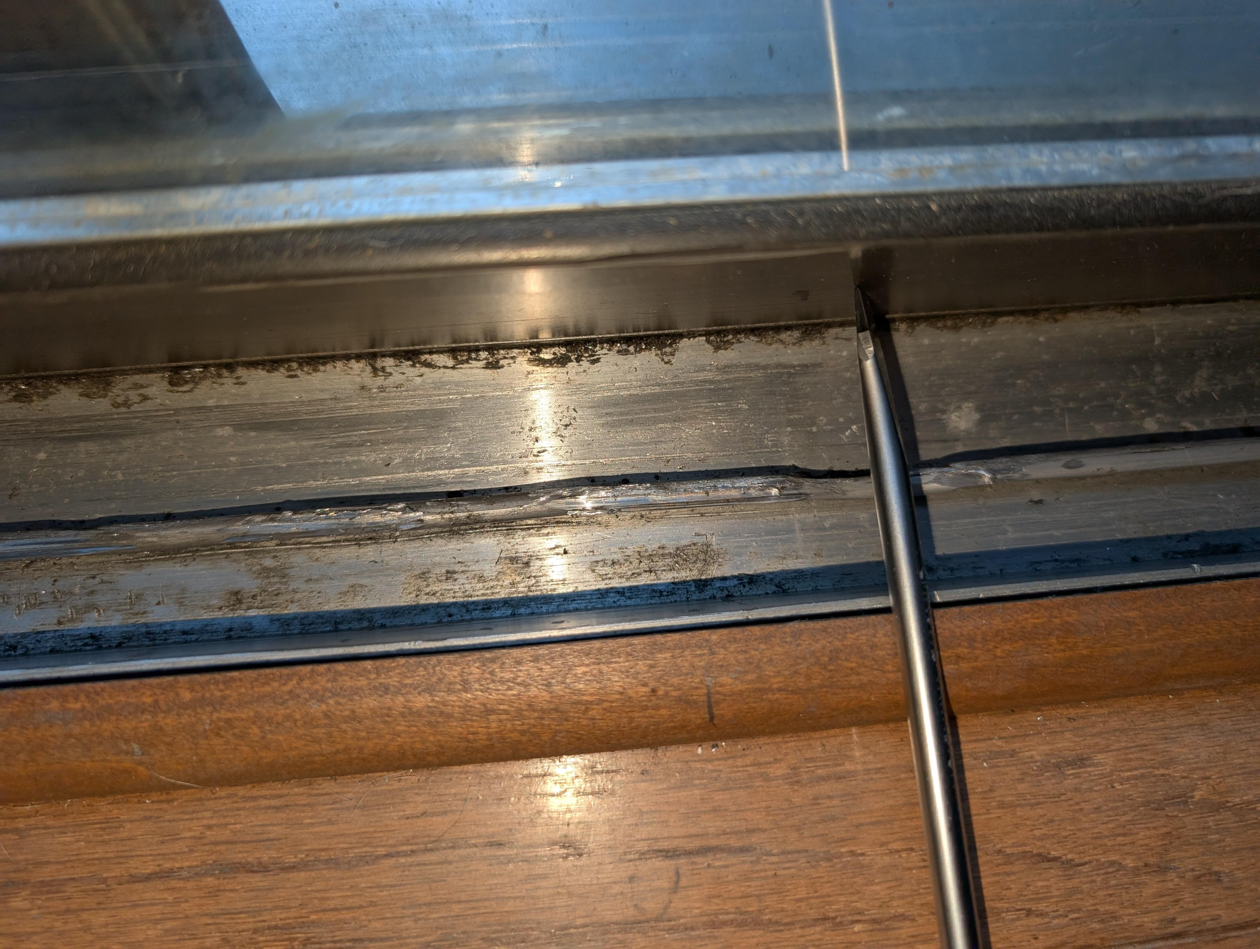 A close-up photo of a metal sliding closet door track with a visible dent and slight bend near one end, indoor lighting