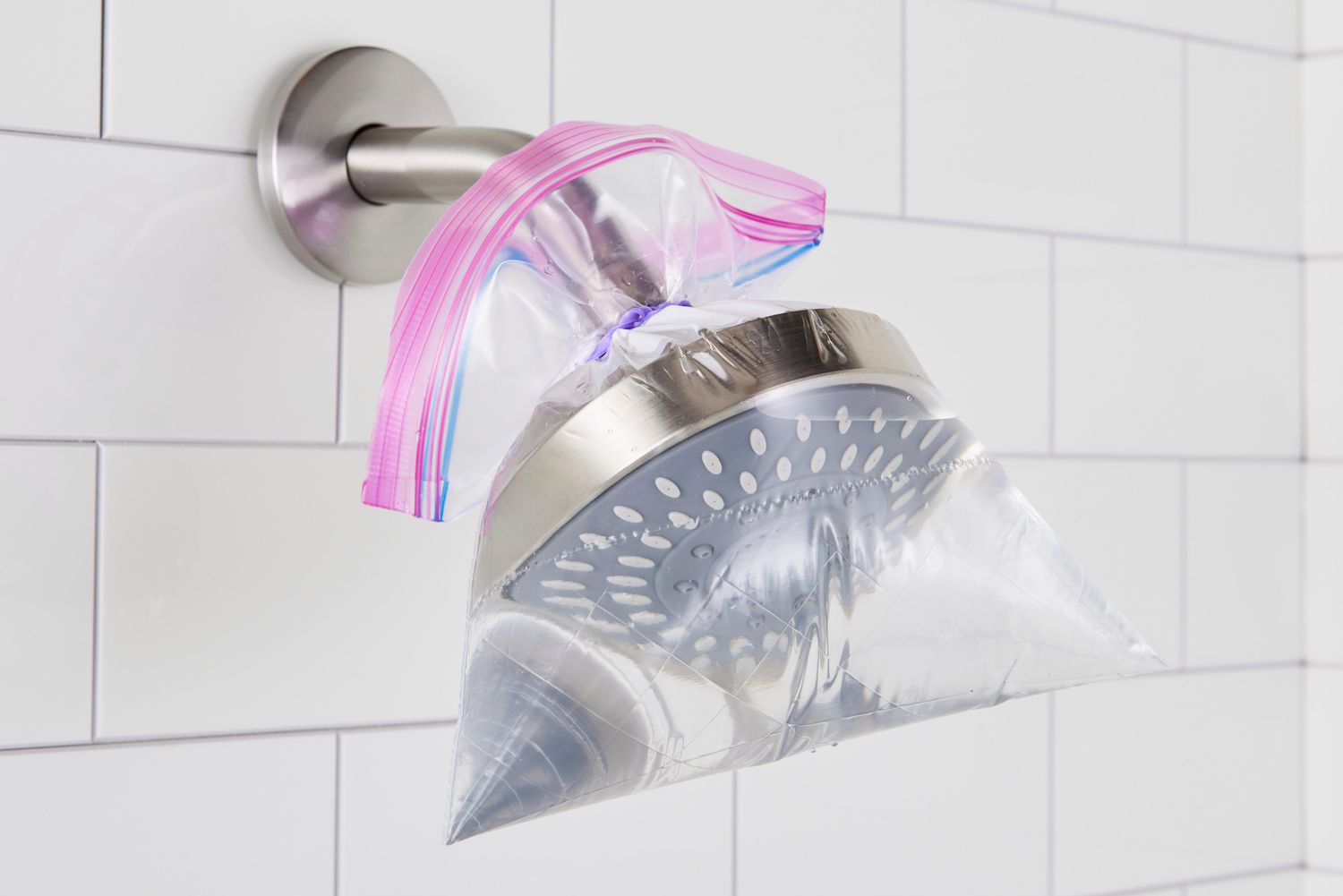 A close-up photo of a showerhead inlet screen being rinsed in a bathroom sink, with a toothbrush and microfiber cloth nearby, realistic photo