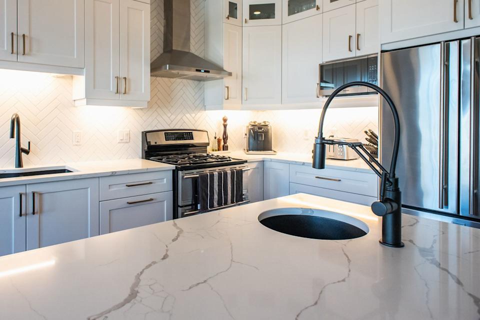 A close-up photo of a small bowl of warm soapy water and a microfiber cloth on a quartz countertop in a modern kitchen