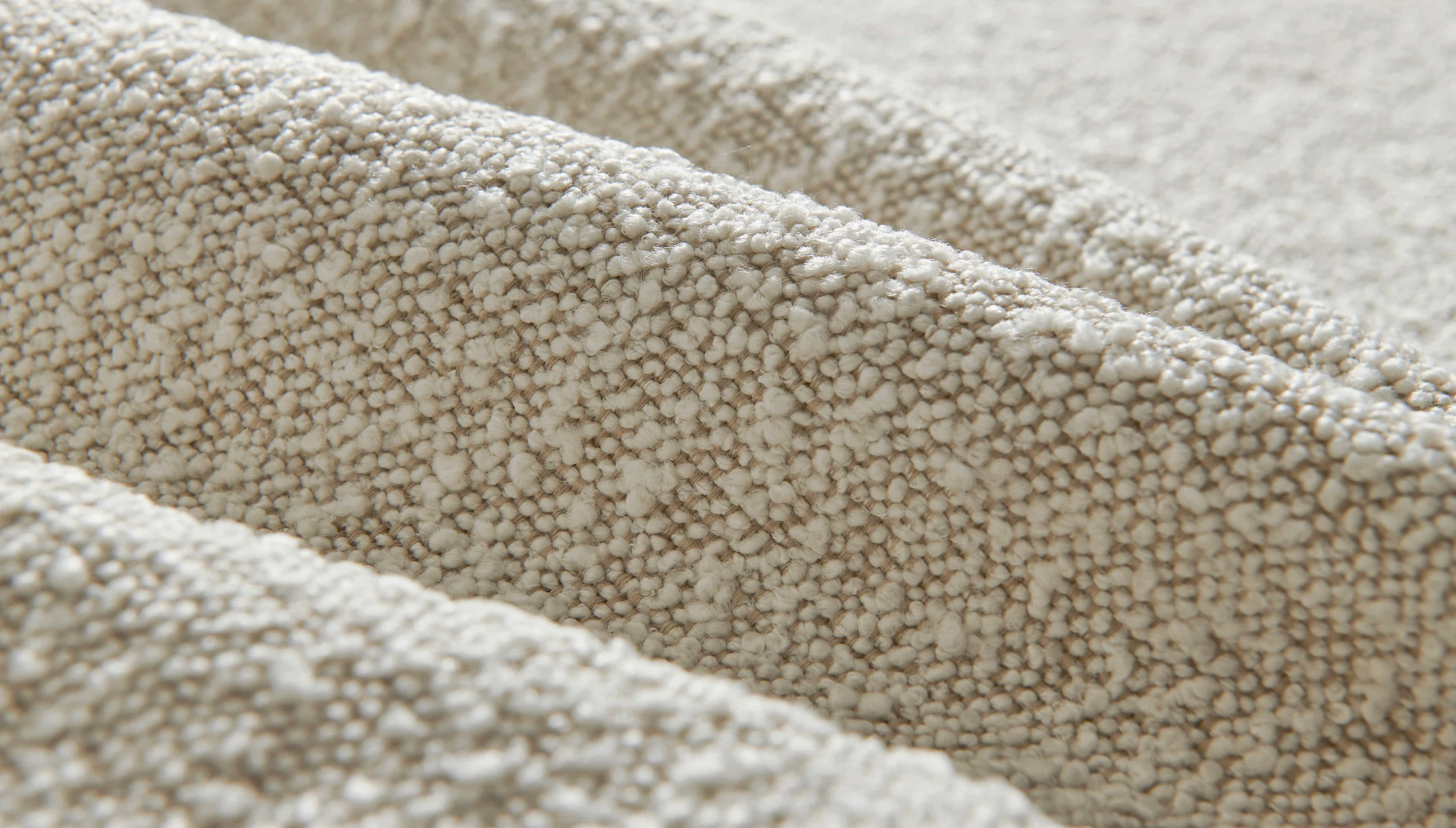 A close-up photo of a soft upholstery brush resting on textured bouclé fabric, showing loops clearly
