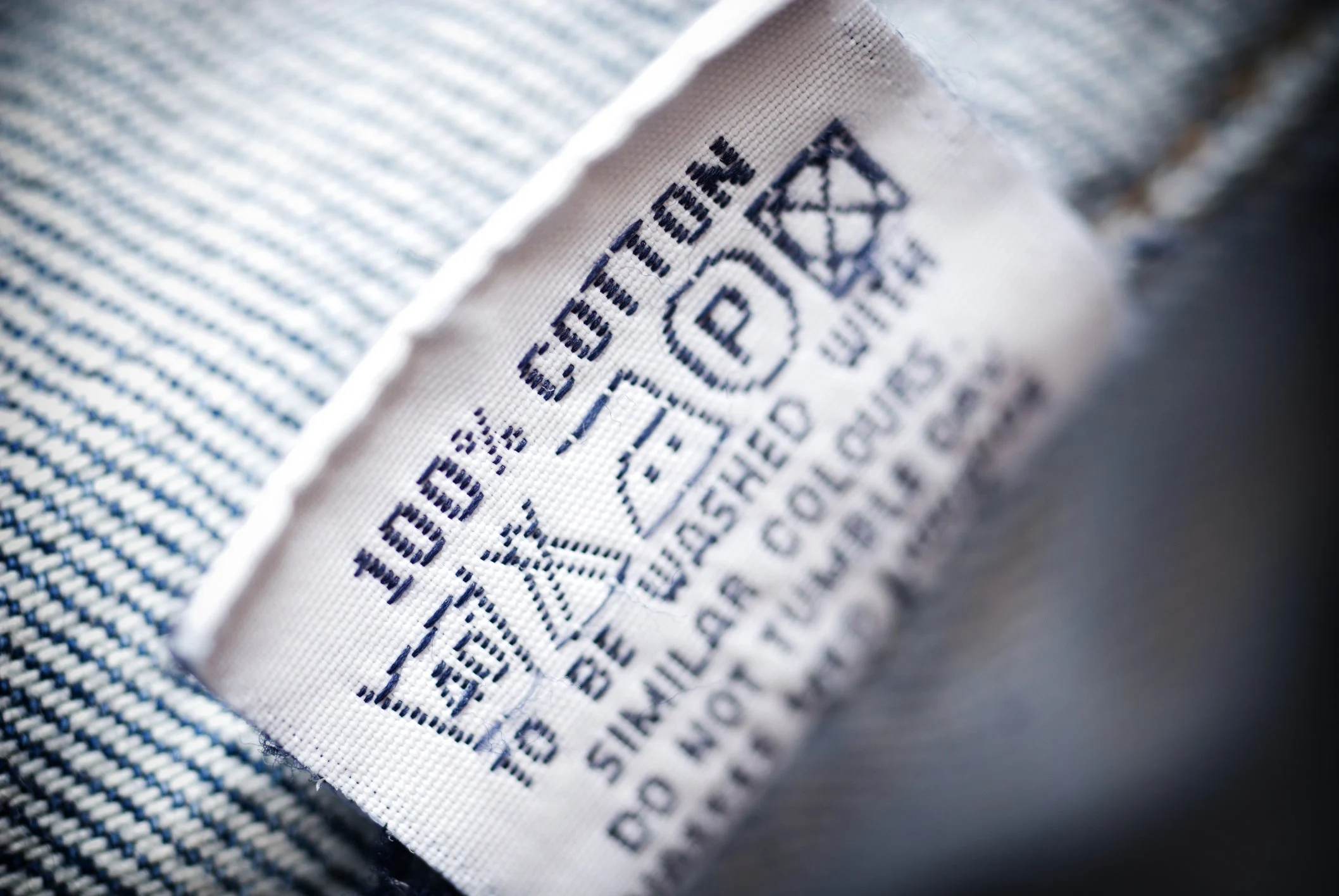A close-up photo of a white curtain care label being held between fingers, showing fabric content and washing symbols