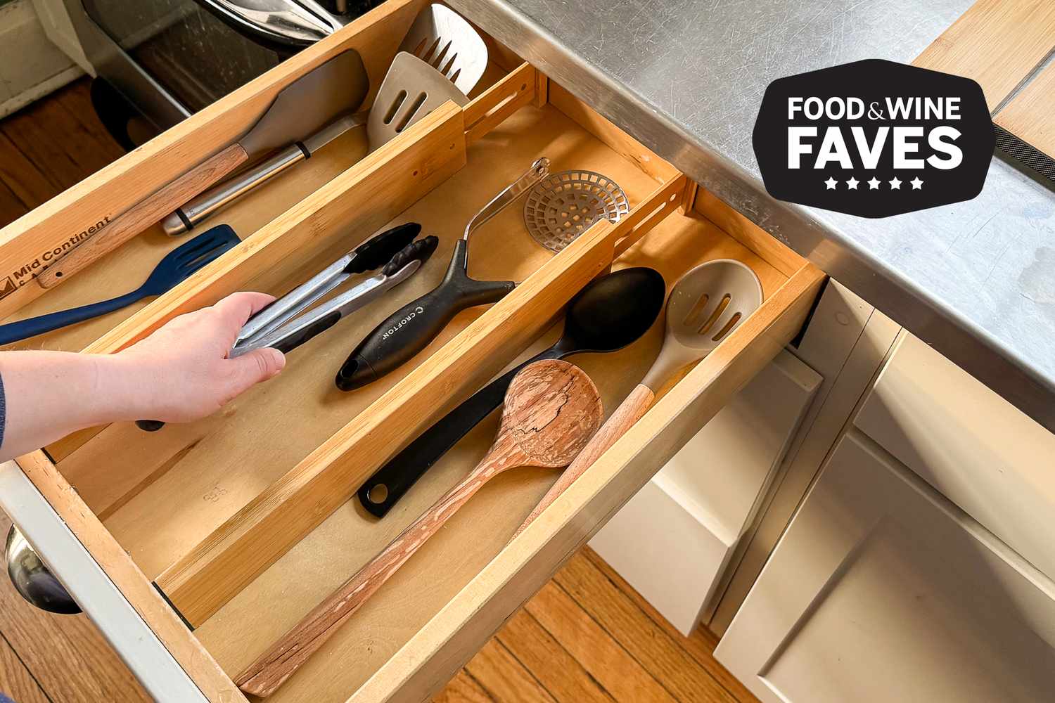 A close-up photo of an organized kitchen utensil drawer with wooden dividers, neatly separated spoons, whisks, tongs, and measuring tools