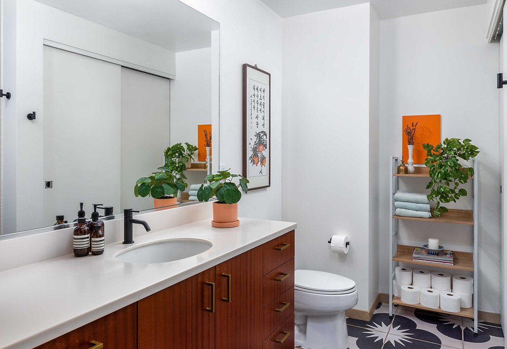 A close-up photo of bathroom wall tile and grout line near a shower corner, showing light staining and a small area of dark mildew at the edge, realistic indoor lighting