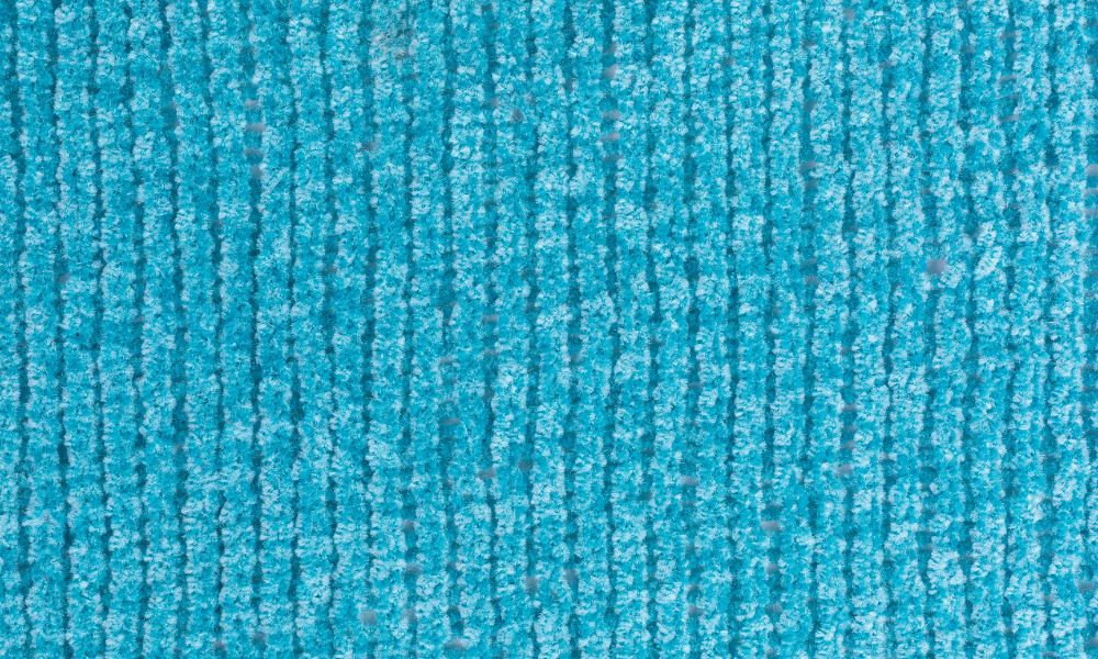 A close-up photo of chenille upholstery fabric showing a soft, raised pile with subtle directional shading, warm indoor lighting