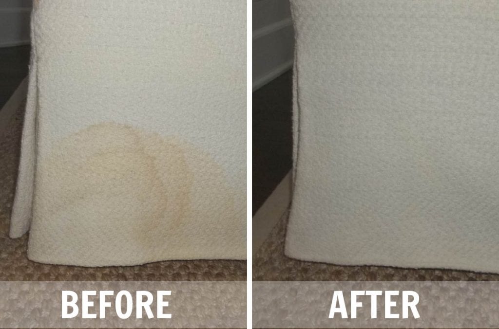 A close-up photo of hands gently blotting a sofa arm with a white microfiber cloth for a small upholstery cleaning test, soft indoor lighting
