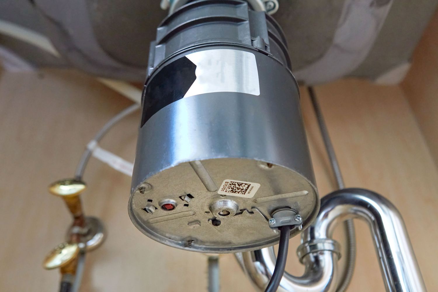 A close-up photo of the underside of a garbage disposal showing a red reset button, cabinet interior visible in the background
