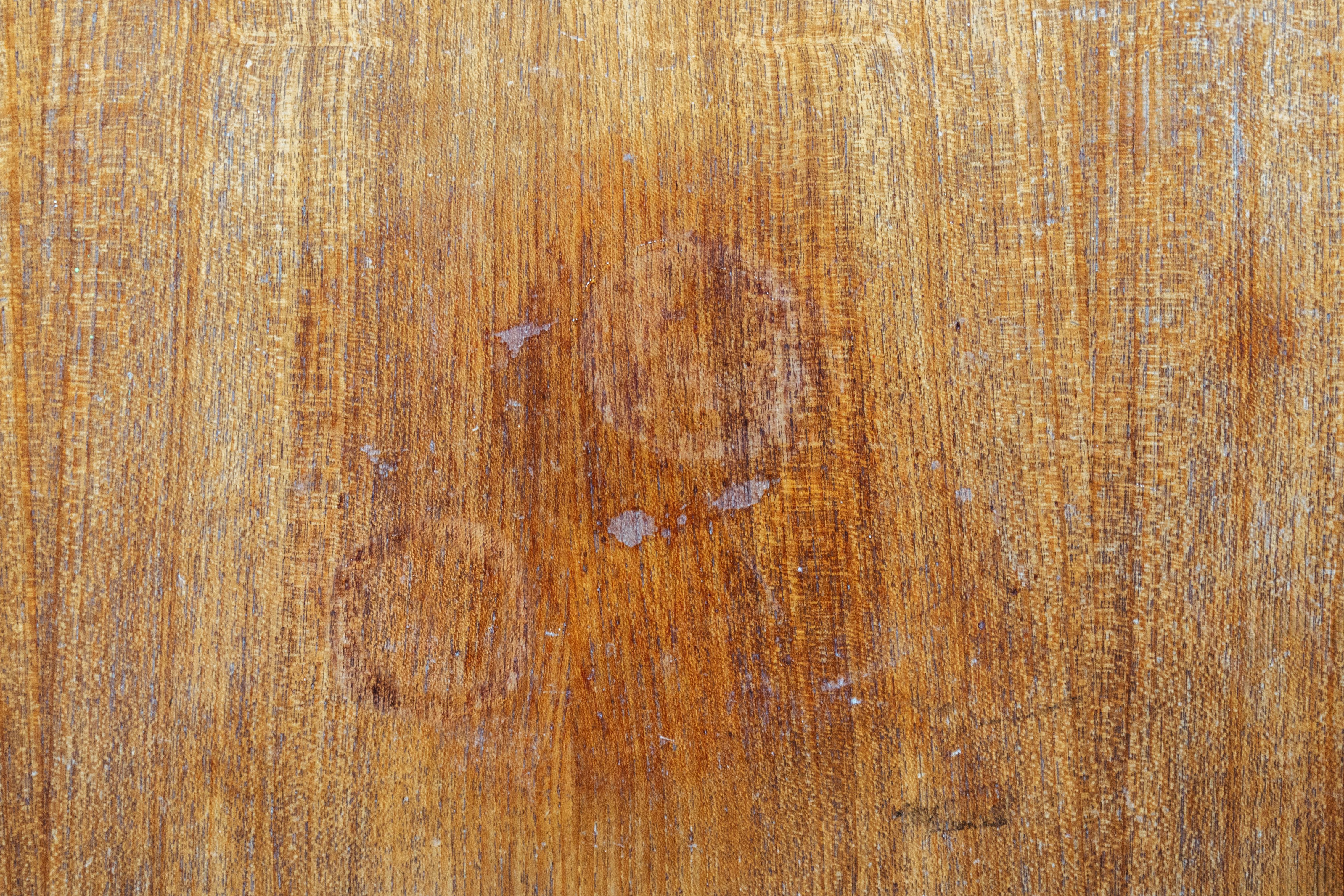 A close up photograph of a cloudy white heat ring on a medium brown wood tabletop with visible grain, soft window light, realistic home setting