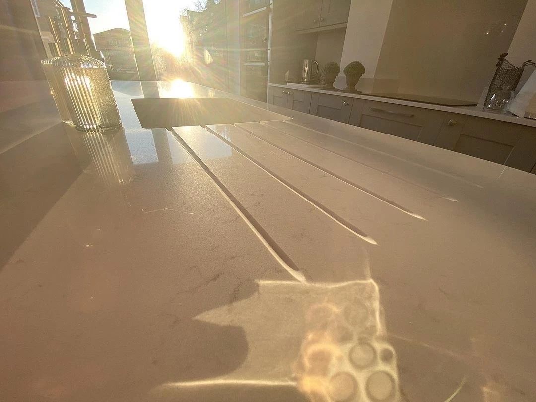 A close-up photograph of water spots and faint mineral rings on a dark quartz countertop beside a stainless steel sink