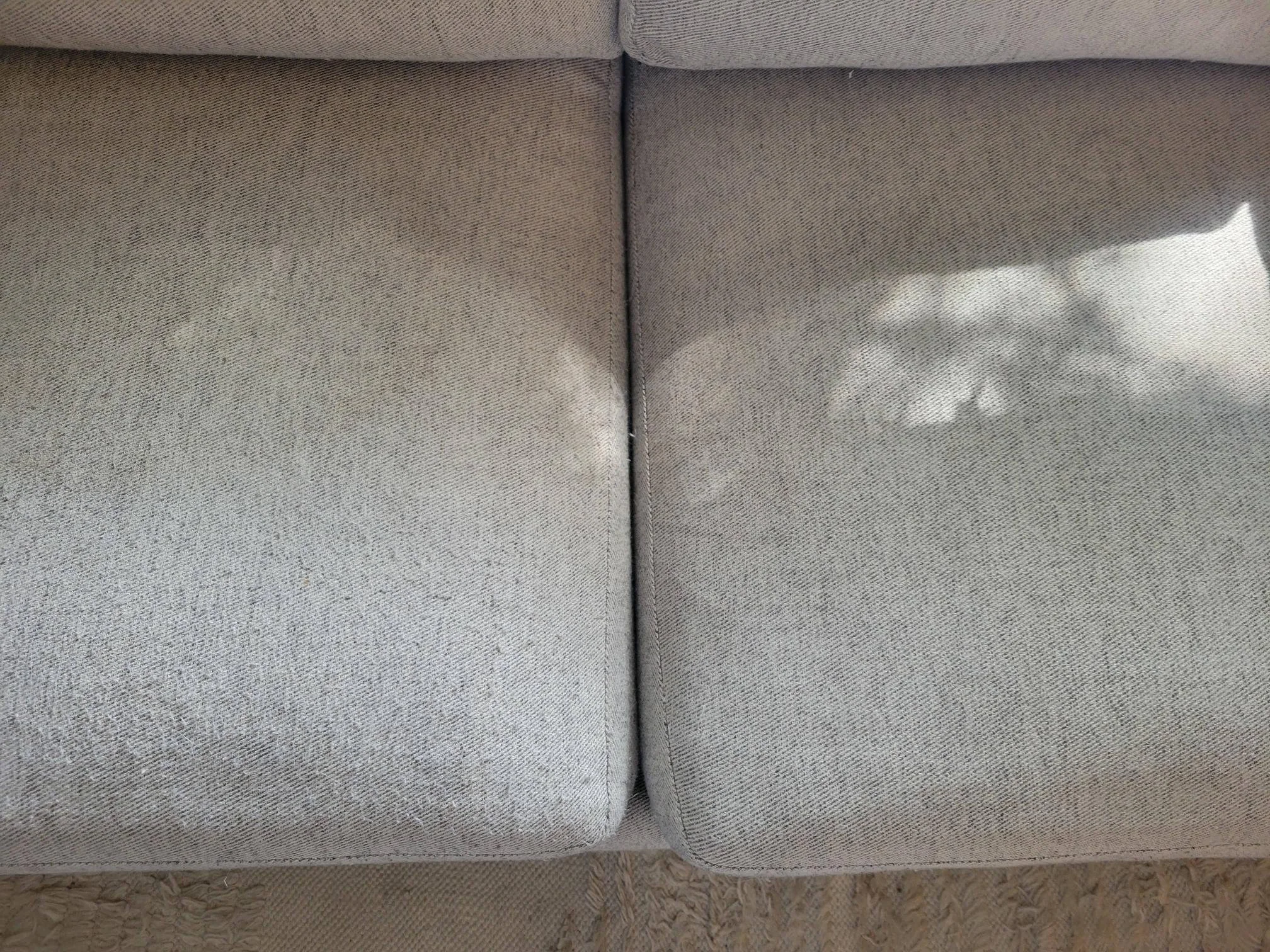 A close-up, real-life photo of a handheld fabric shaver gently removing pilling from a textured fabric sofa cushion in warm natural light