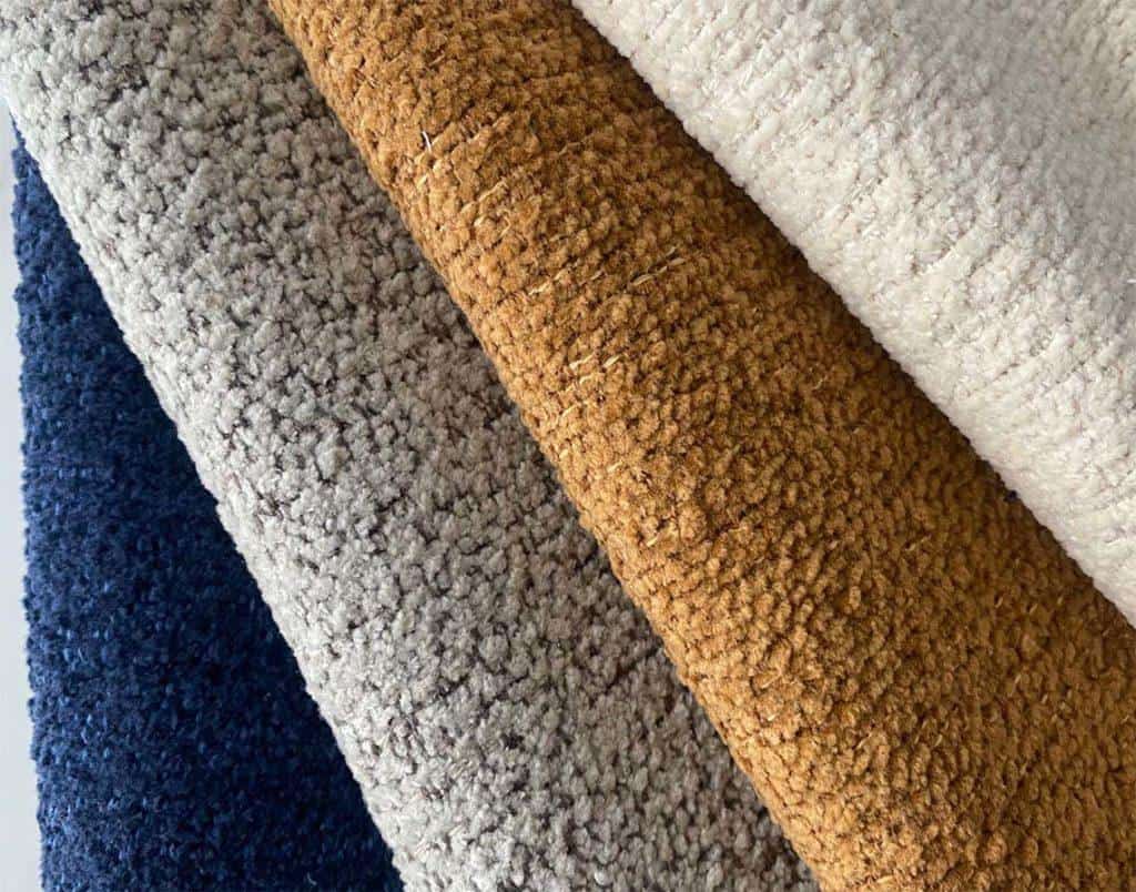 A close-up real photo of hands gently blotting a fresh spill on a light-colored performance fabric sofa cushion with clean white microfiber cloths in soft natural window light