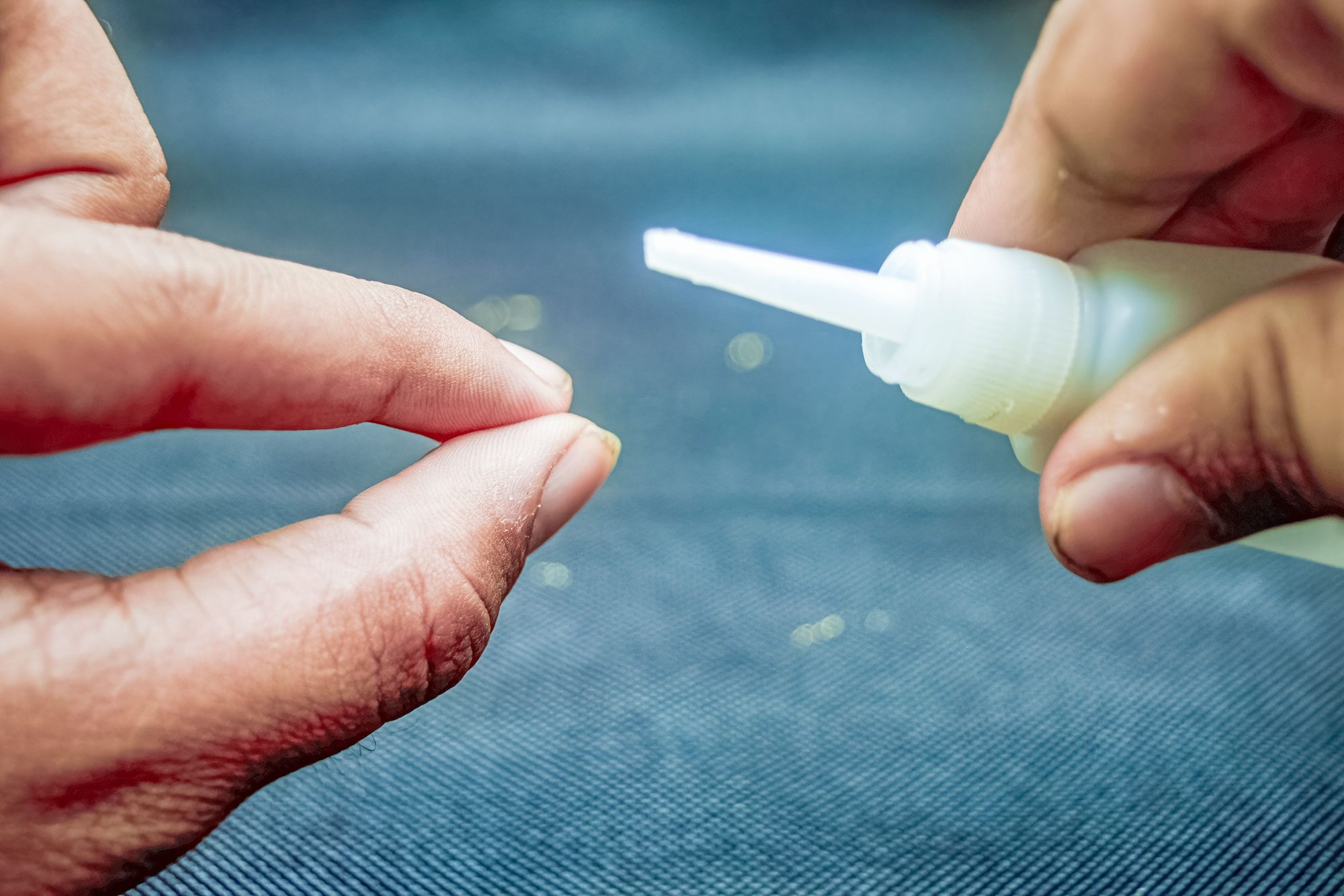 A close-up real photograph of hands using a plastic scraper to lift dried glue from a beige woven fabric sofa cushion, natural window light, cleaning supplies nearby