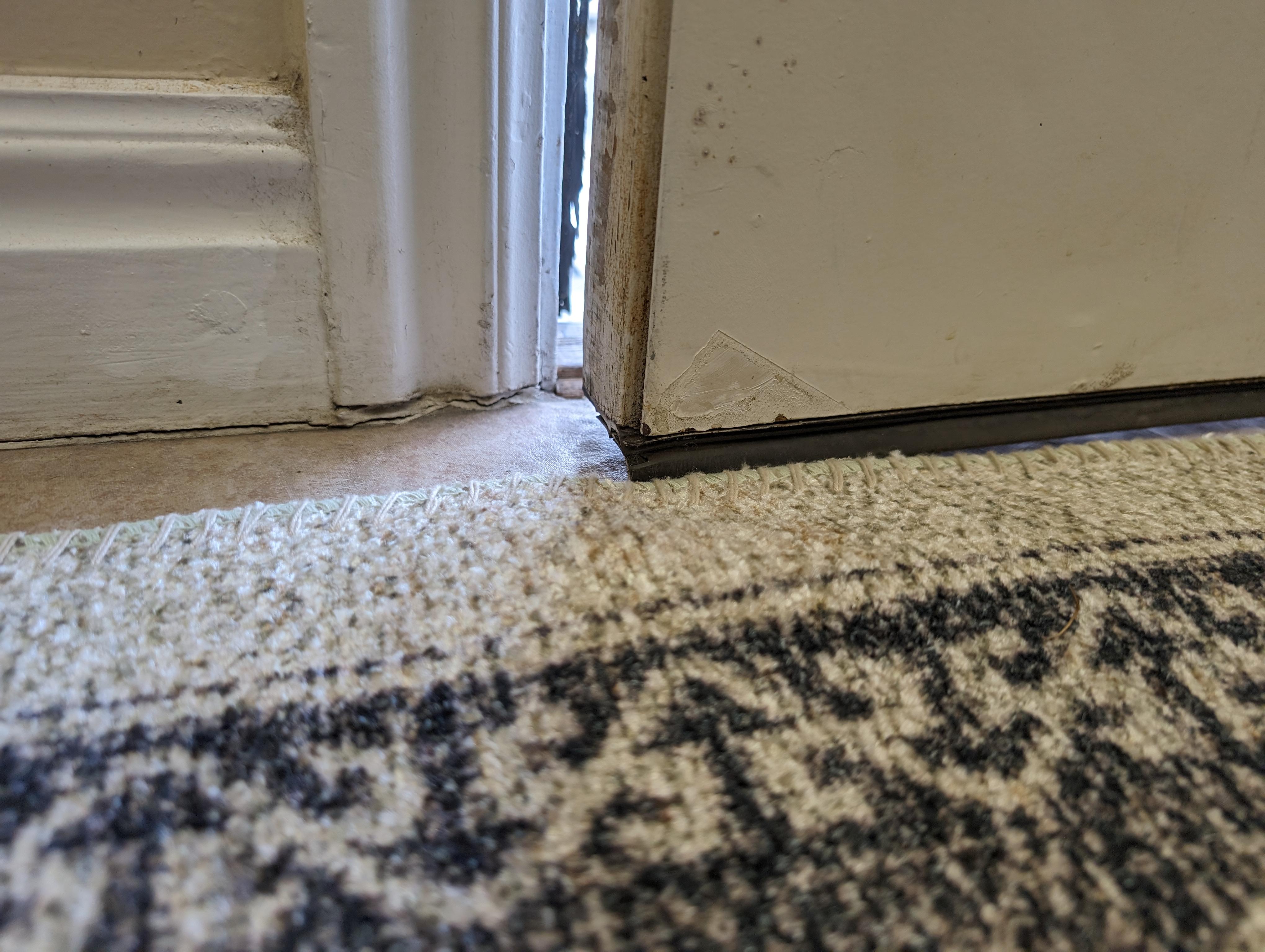 A close view of the bottom edge of an interior door hovering just above a thick rug edge that is slightly raised