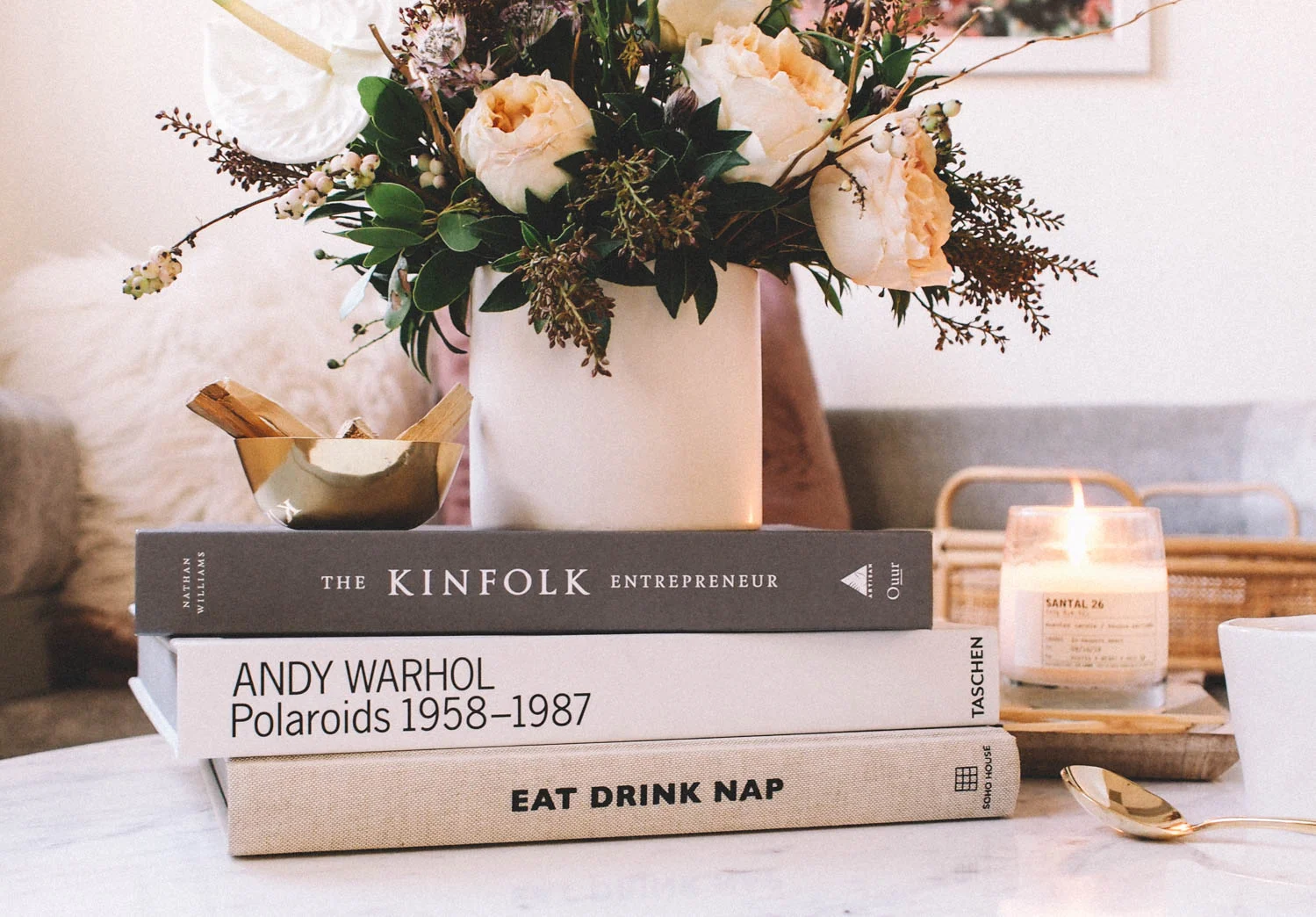 A coffee table styled with one tray, two stacked books, a tall vase with leafy branches, and a framed photo in natural light