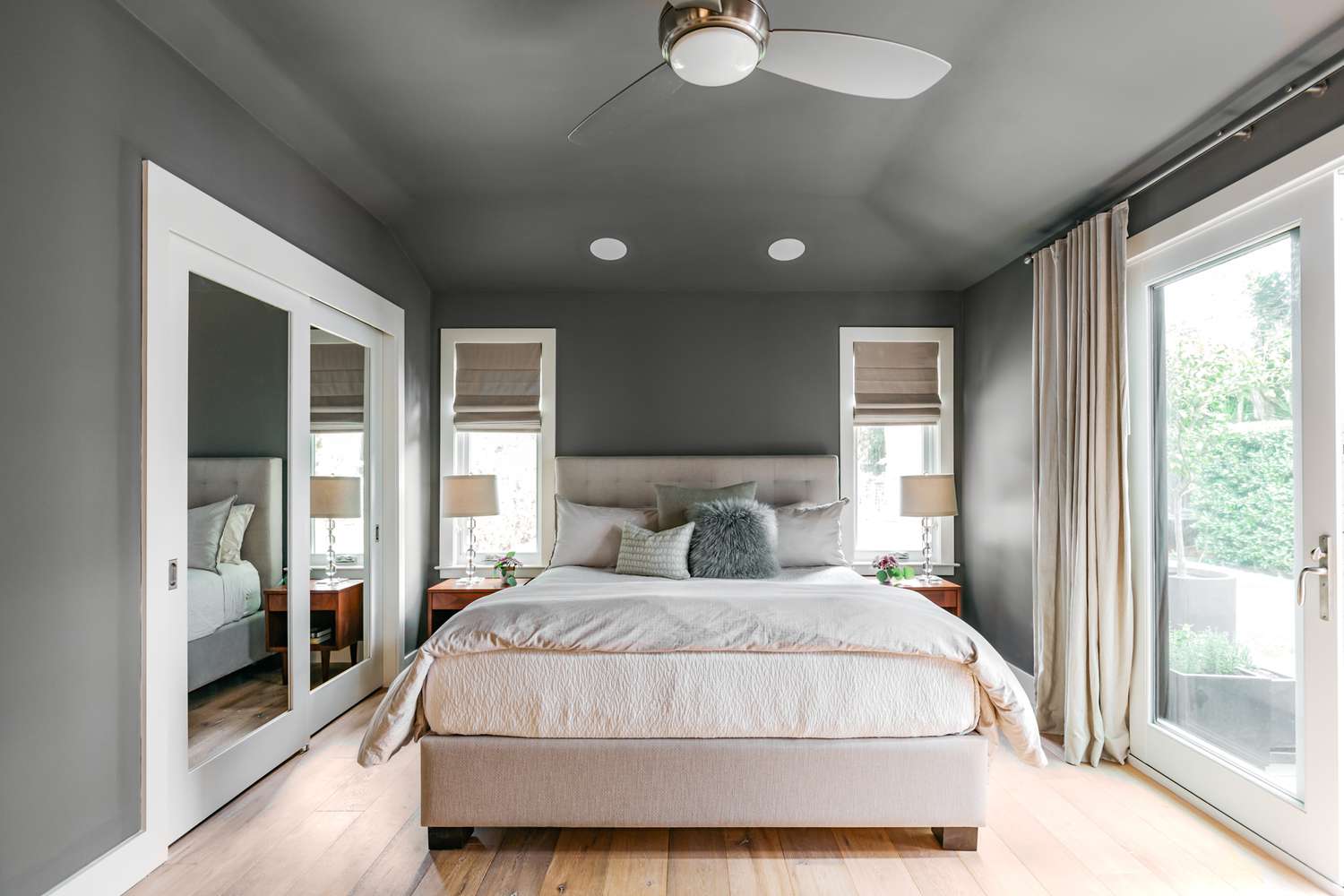 A cozy bedroom with a low ceiling painted a deep matte color, mid-tone walls, layered bedding, and warm bedside lamps, realistic interior photography style