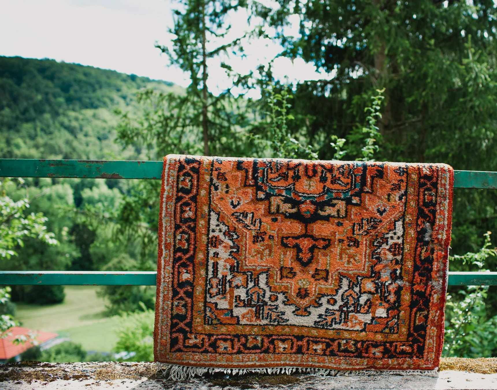 A freshly unrolled area rug laid flat on top of clean towels in a bright room, with a small fan nearby to help it dry