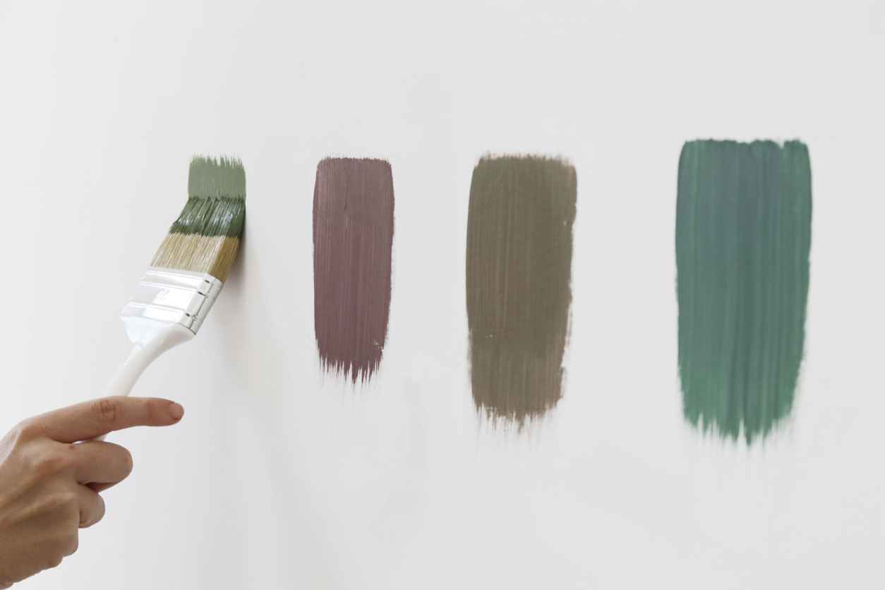A hand using a small paint roller to apply a neat test swatch on a white wall in a home, with natural light coming through a nearby window, realistic home photography style