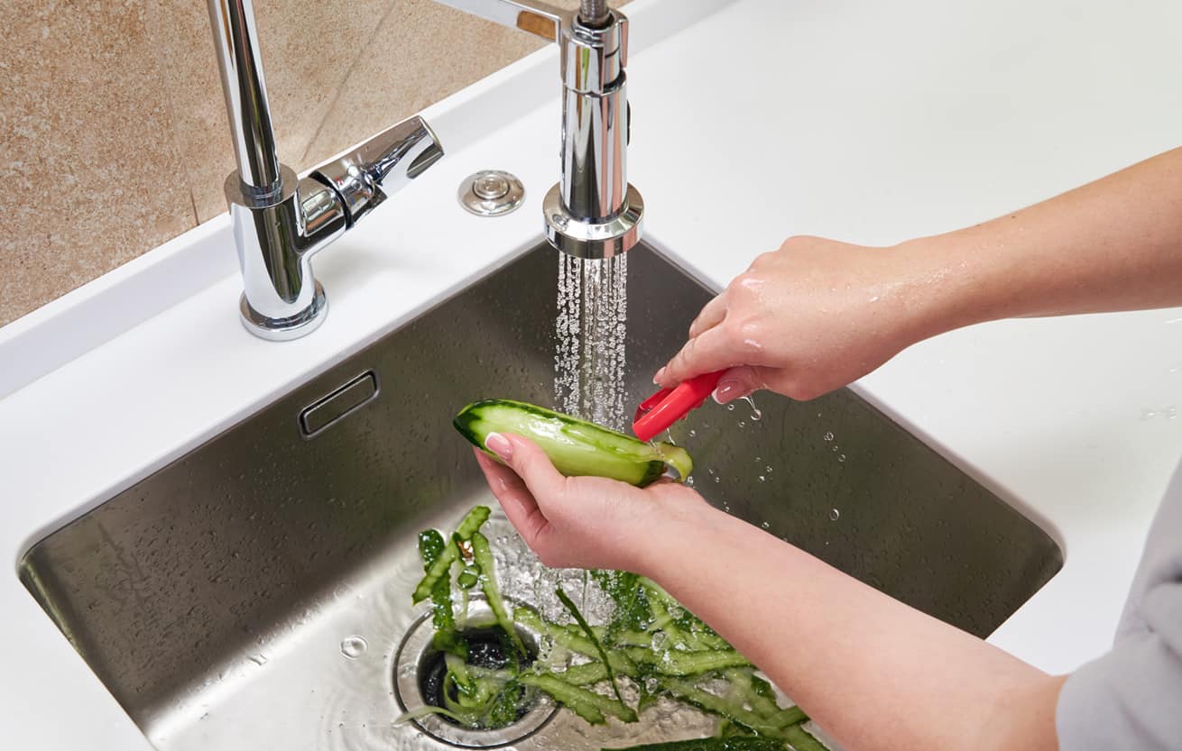 A kitchen faucet running cold water into a sink with a garbage disposal drain opening, bright natural light and everyday home setting