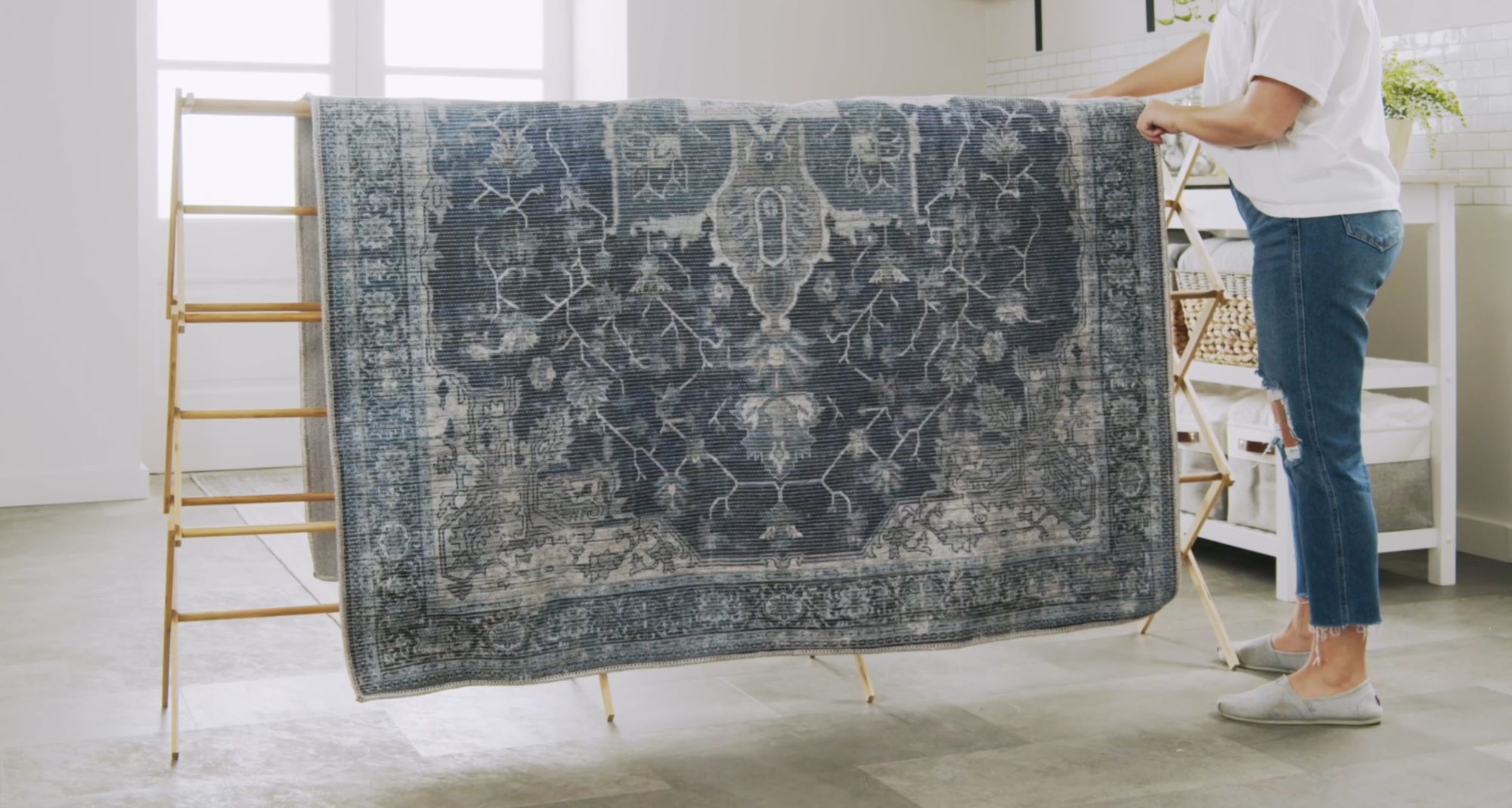 A large area rug draped over a wooden porch railing to air out, with the rug hanging evenly and the fringe visible