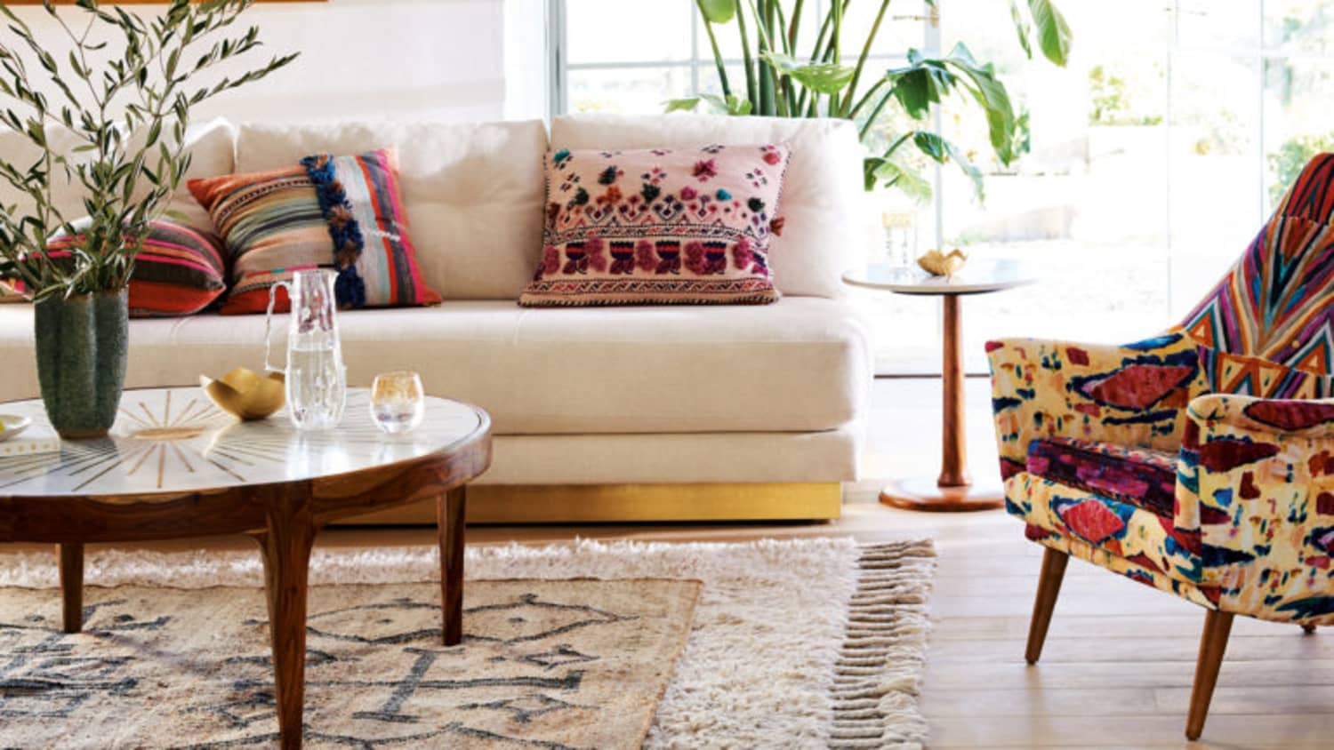 A living room with a large natural rug layered under a smaller patterned rug, anchoring a sofa and two chairs