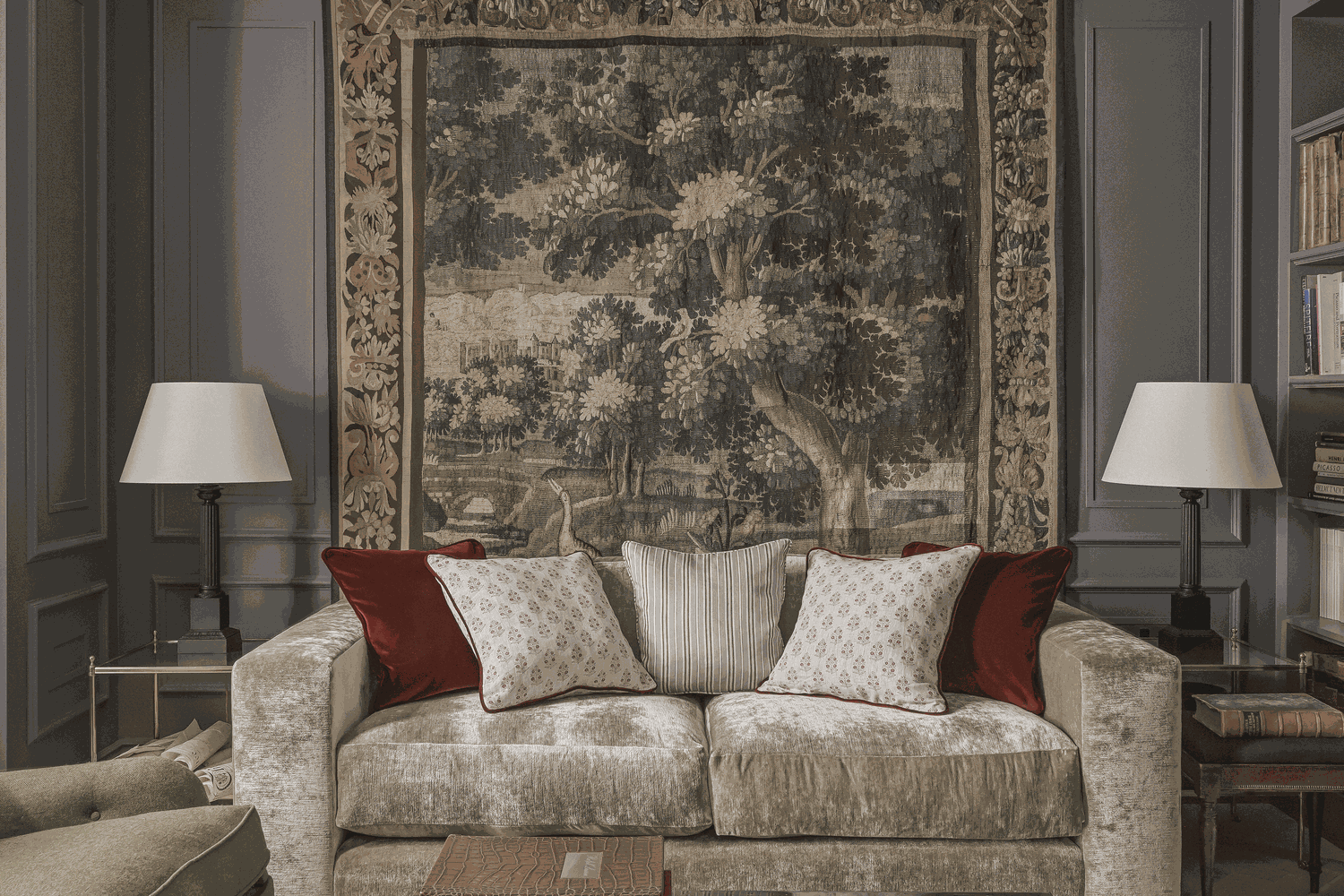 A living room with a large woven tapestry hung behind a sofa, layered neutral pillows, and warm evening lighting, realistic interior photograph