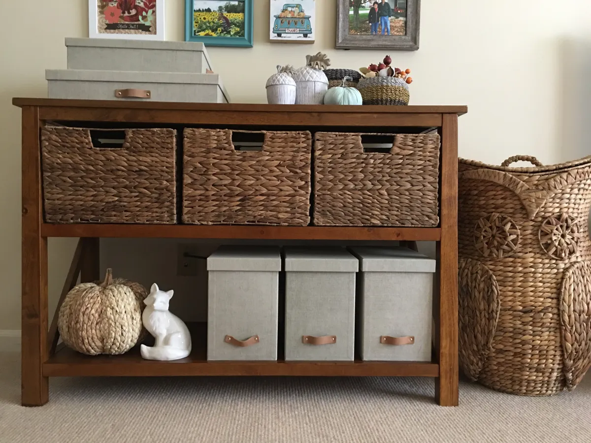 A media console with a lidded box for remotes and a woven basket beside it holding folded throws