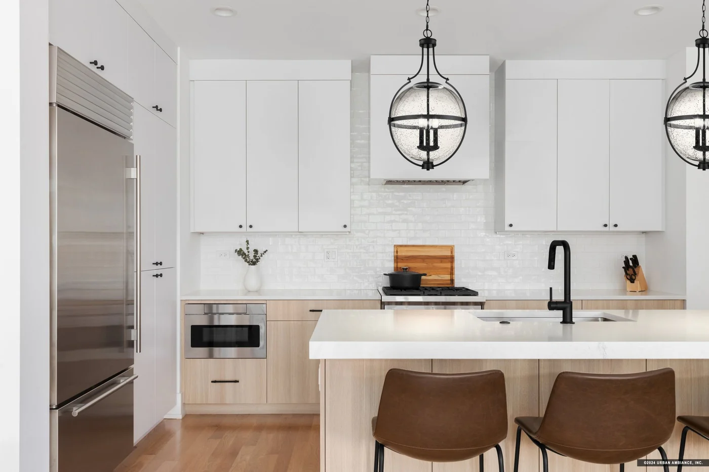 A modern kitchen with brass dome pendant lights over a marble island, stainless steel appliances, and matte black cabinet pulls in bright natural daylight