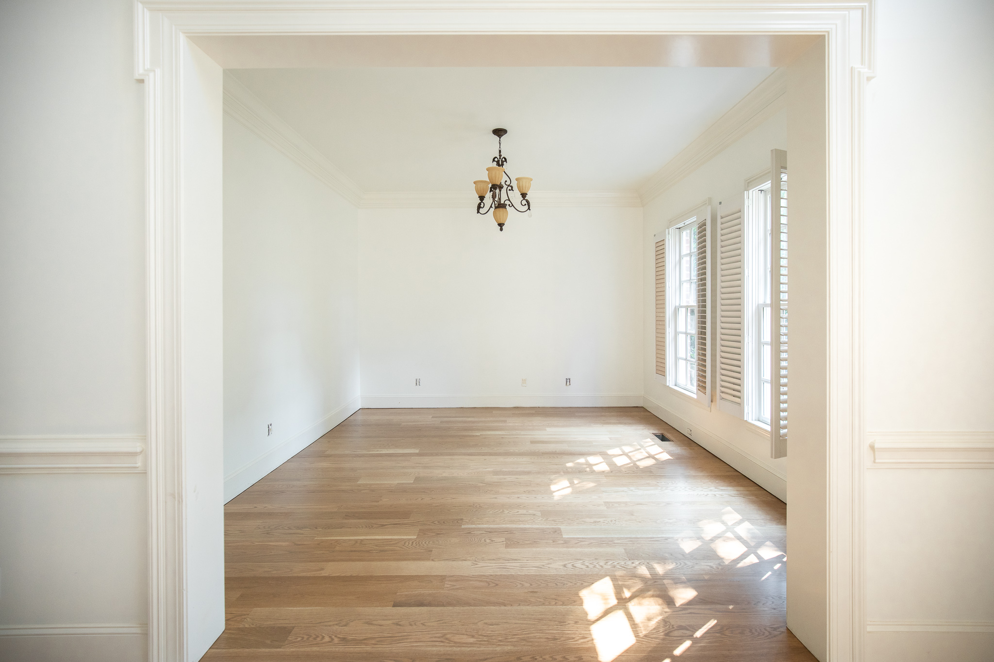 A narrow hallway with vintage oak floors, warm white walls, an antique mirror with patina, and a small brass sconce casting a golden glow