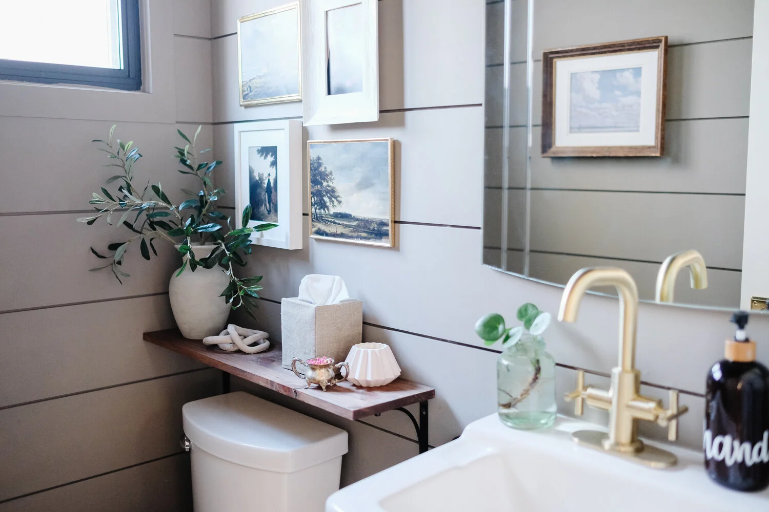 A narrow powder room with peel-and-stick wallpaper on the sink wall only, a simple white vanity, and a small round mirror centered above the faucet