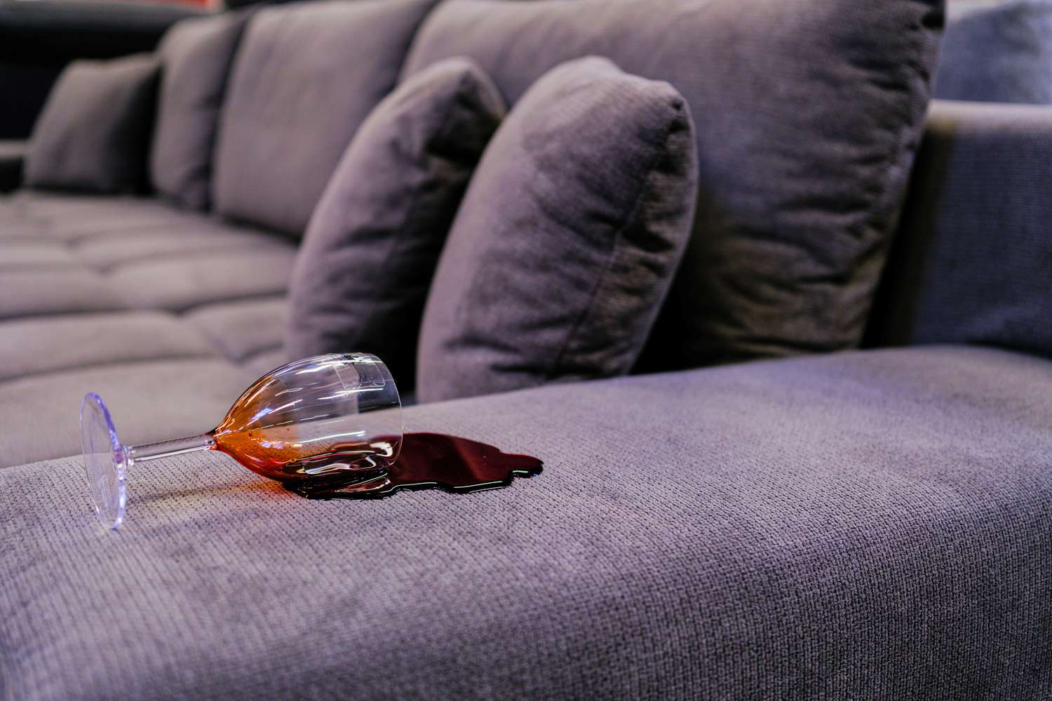 A person blotting a small red wine spill on a navy velvet sofa with a white microfiber cloth