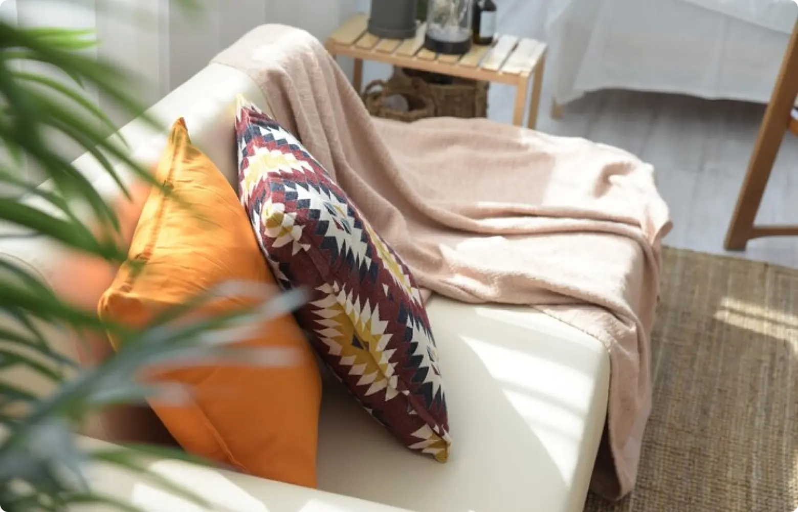 A person draping a soft cotton throw blanket over the arm of a light-colored fabric sofa in a sunlit apartment