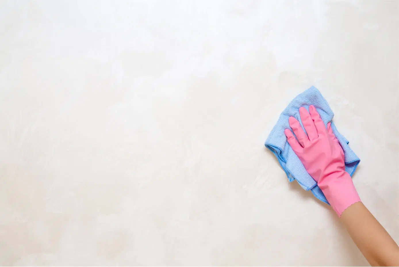 A person gently wiping a light-colored painted wall with a clean microfiber cloth near a baseboard, real home interior photo