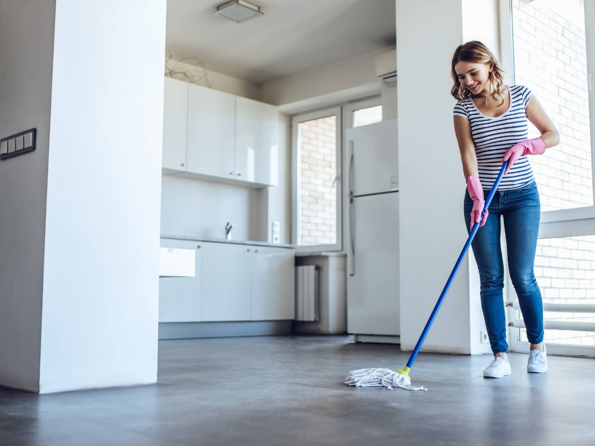A person in a mostly empty apartment gently wiping scuff marks from a white wall with a microfiber cloth, moving boxes in the background, real photo
