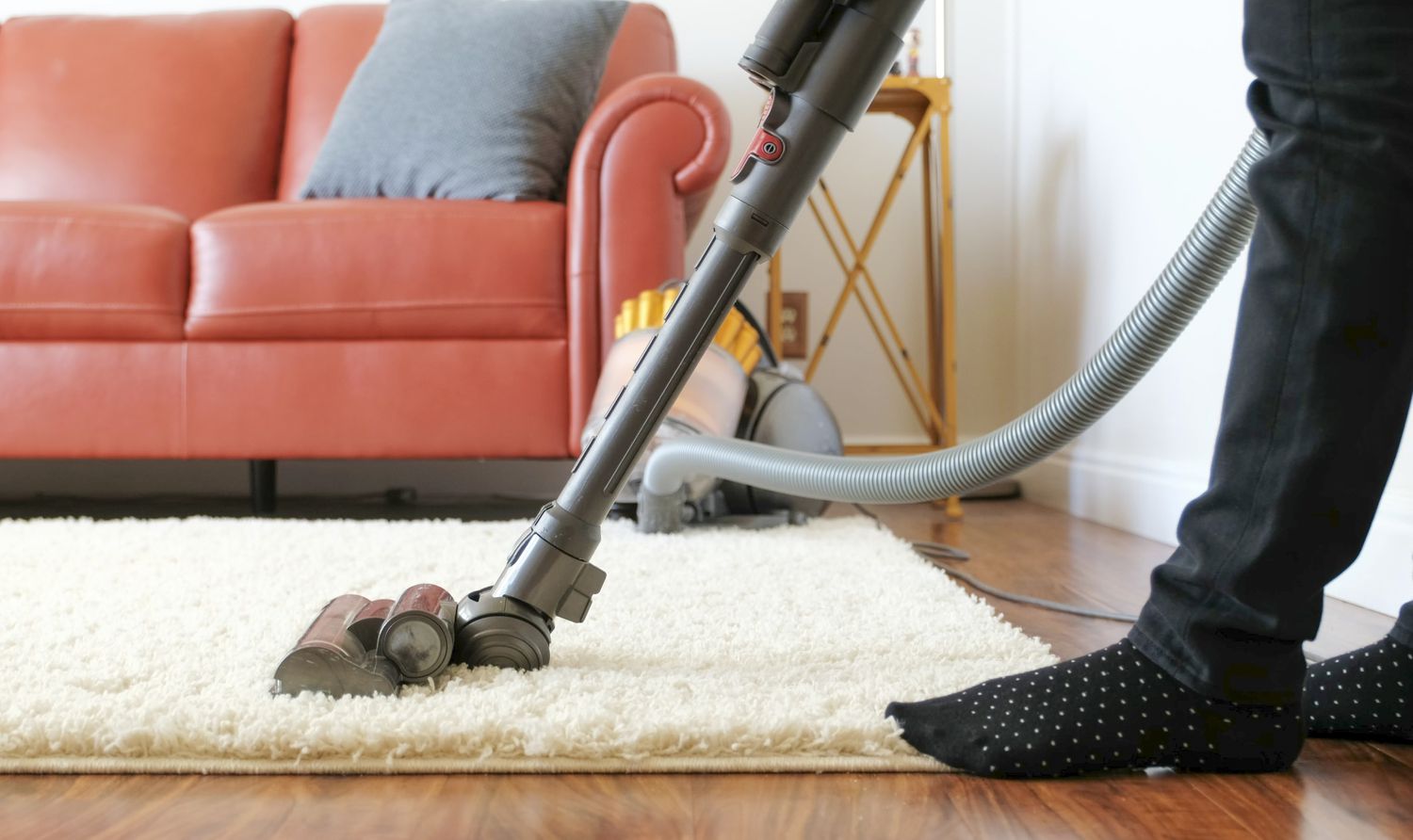 A person vacuuming a high pile area rug with a vacuum set to gentle suction, the vacuum head gliding over textured fibers in a cozy home