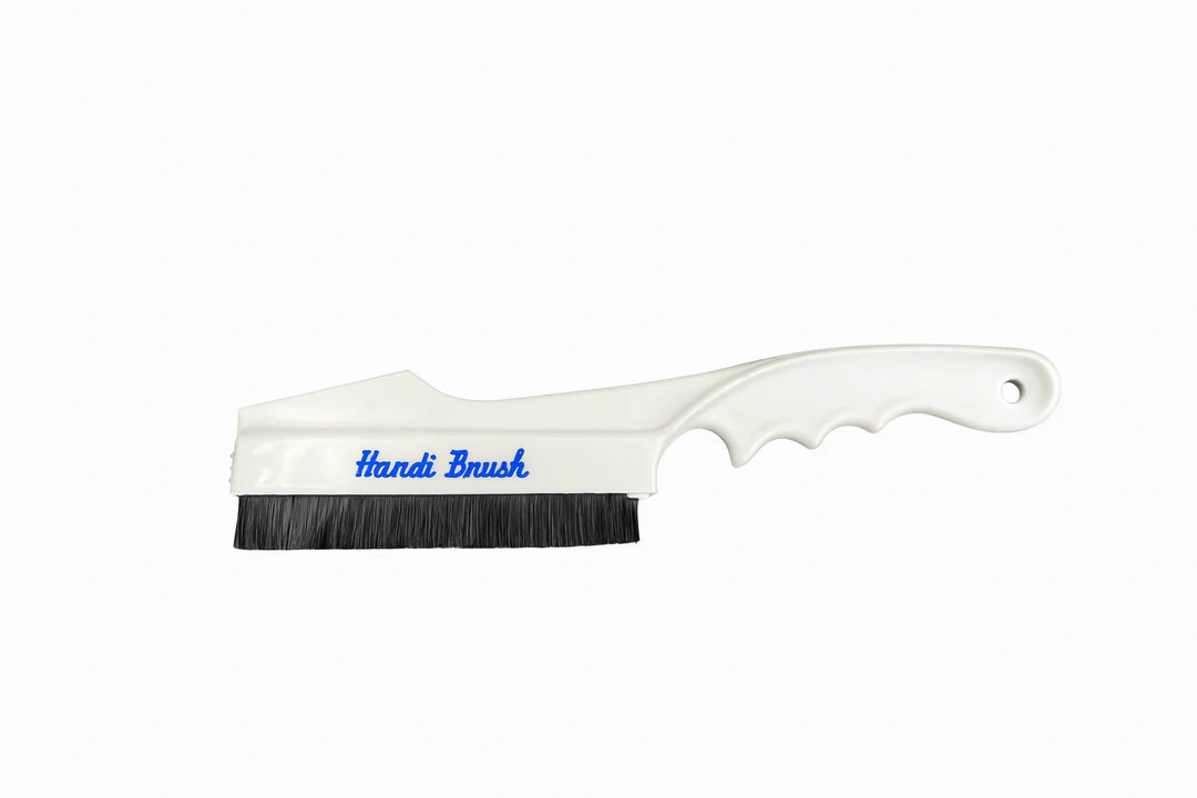 A photo of a hand gently brushing a dry chenille sofa arm with a soft upholstery brush in one direction, evening light, cozy living room