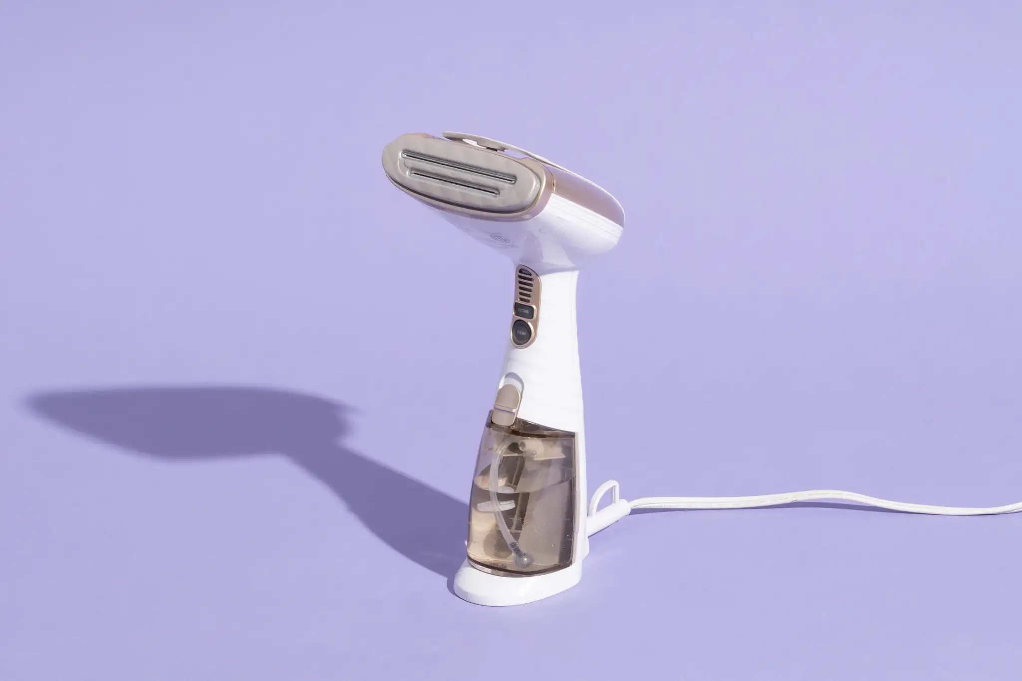 A photo of a handheld garment steamer being used a few inches above a green corduroy sofa cushion to lift flattened wales, with the nozzle angled away and soft daylight in the room