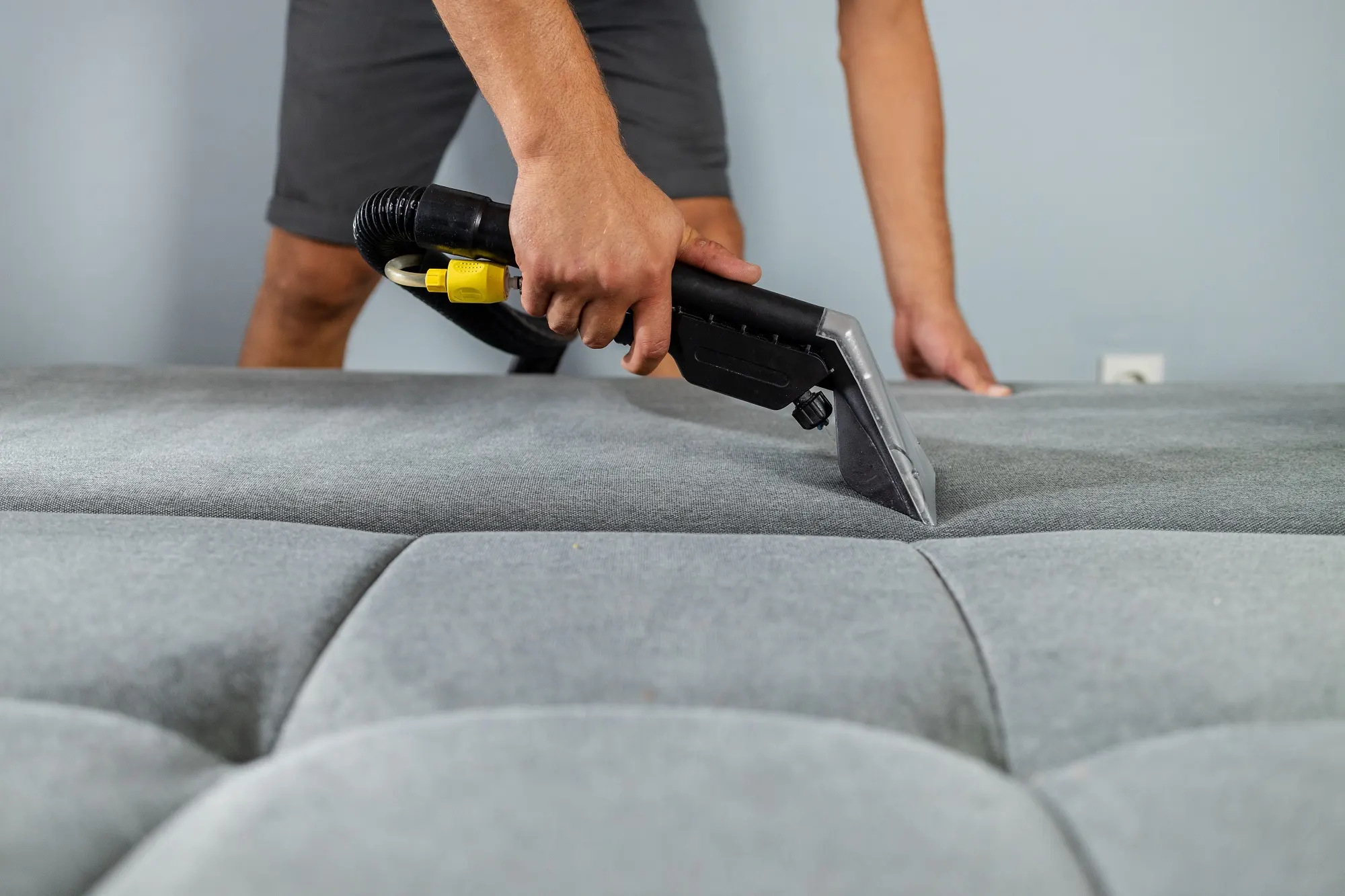 A photo of hands using a cotton swab to patch test cleaner on a hidden seam under a sofa cushion, close-up, soft indoor lighting