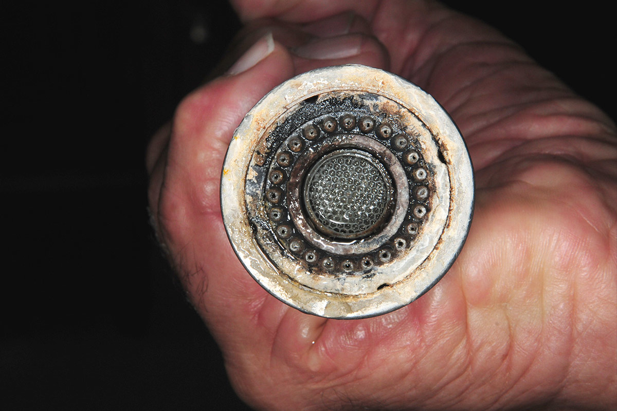 A real close-up photo of a pull-down kitchen faucet sprayer head with visible white mineral buildup around the spray holes
