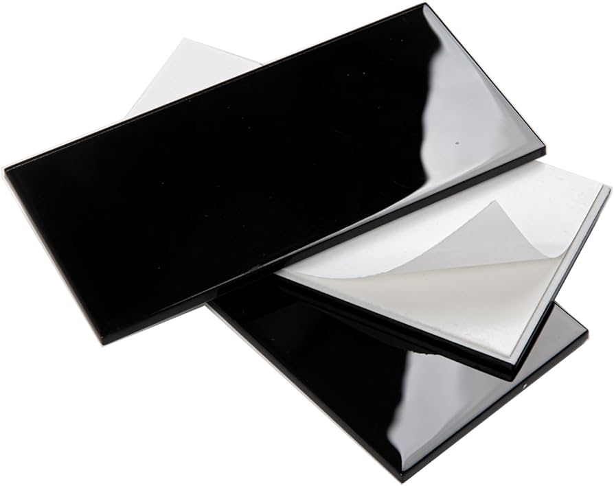 A real photo close-up of a glossy glass-look peel-and-stick backsplash tile in a soft smoky gray, reflecting under-cabinet lighting above a quartz-look countertop